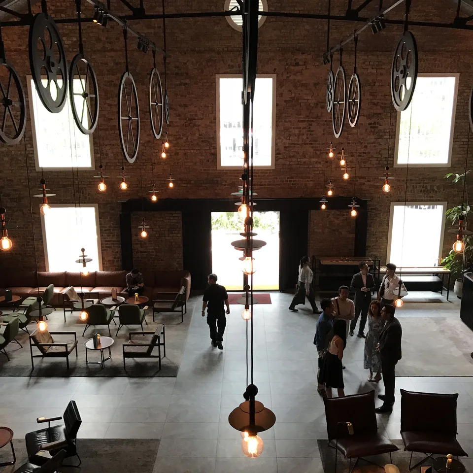 The lobby in daylight from above, brick walls and roof trusses, people standing in the open floor