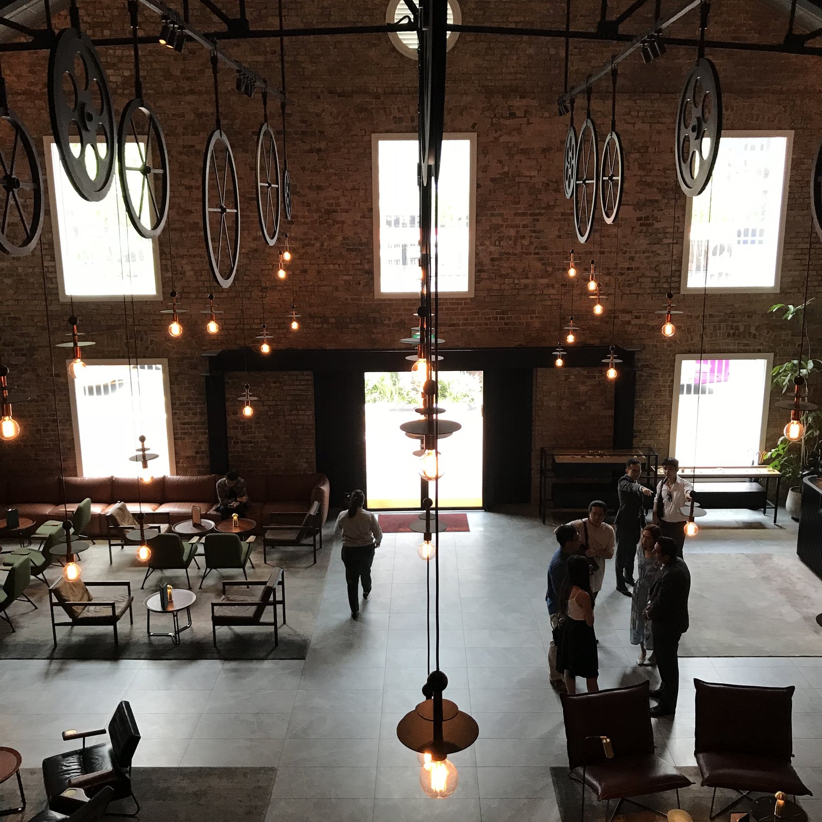 The lobby in daylight from above, brick walls, roof trusses, pendant bulbs and low chairs on the open floor