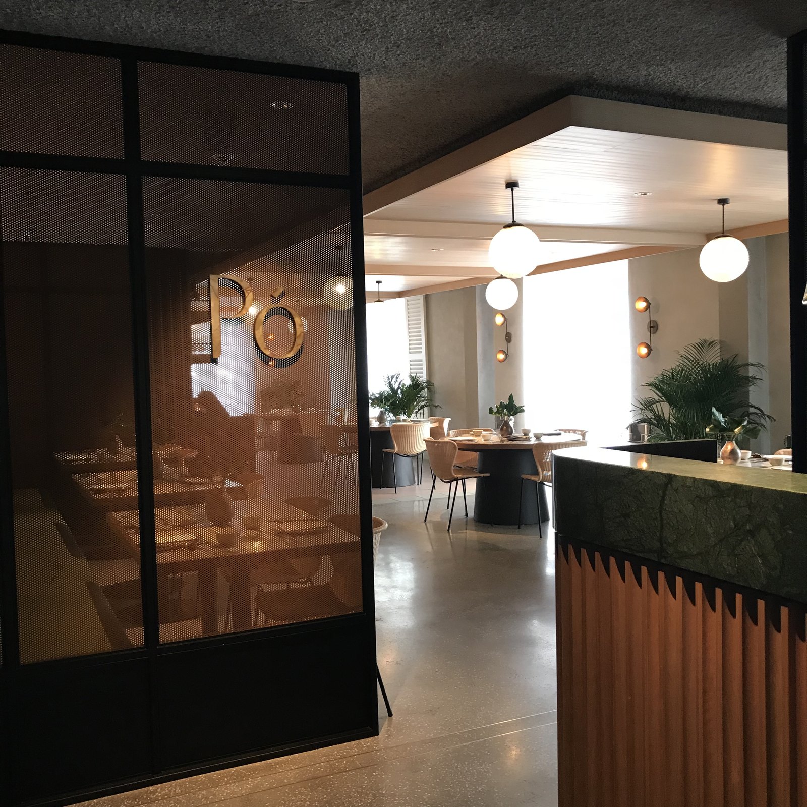 The restaurant seen from the lobby through a black steel and glass screen, tables and pendant lights beyond