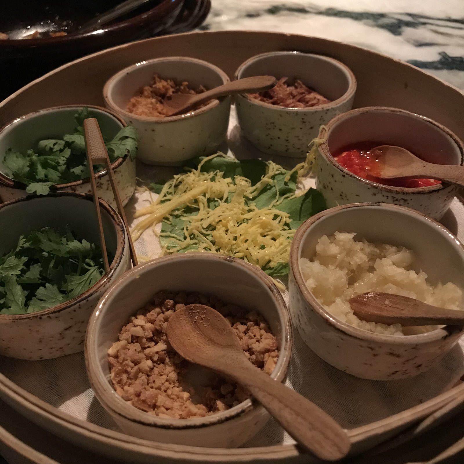 Small bowls of popiah fillings in a steamer basket, with wooden spoons in each