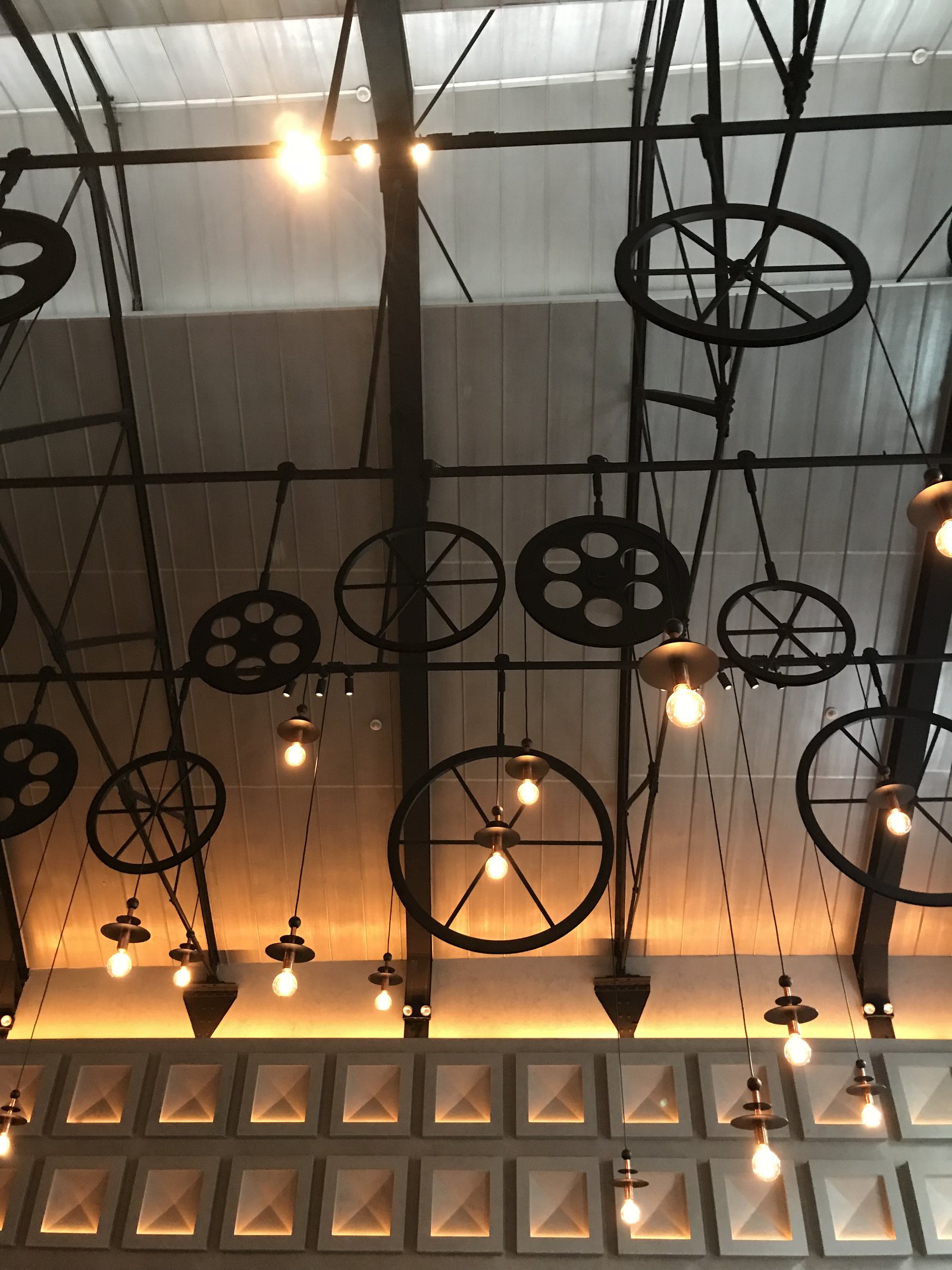 Cast-iron pulley wheels and pendant bulbs hanging on rods from the roof structure, the lit wall of recessed boxes below