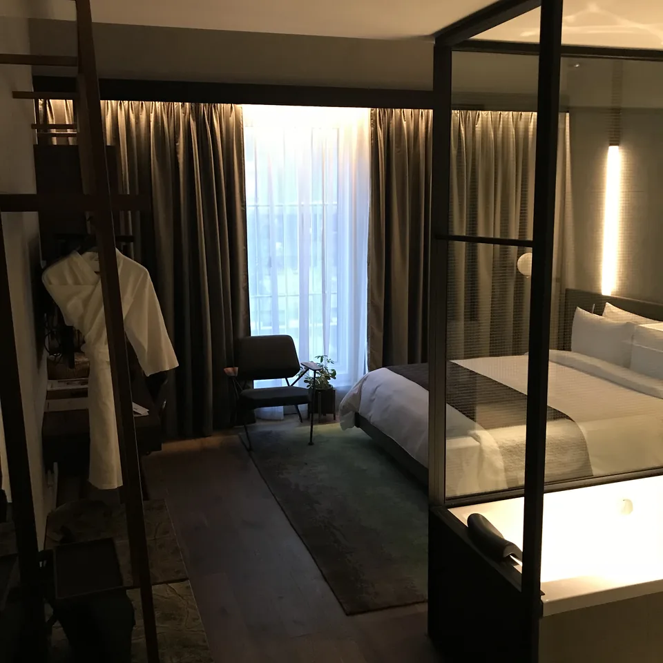The room from the doorway, a four-poster steel frame around the bed and a glazed bathroom wall beyond