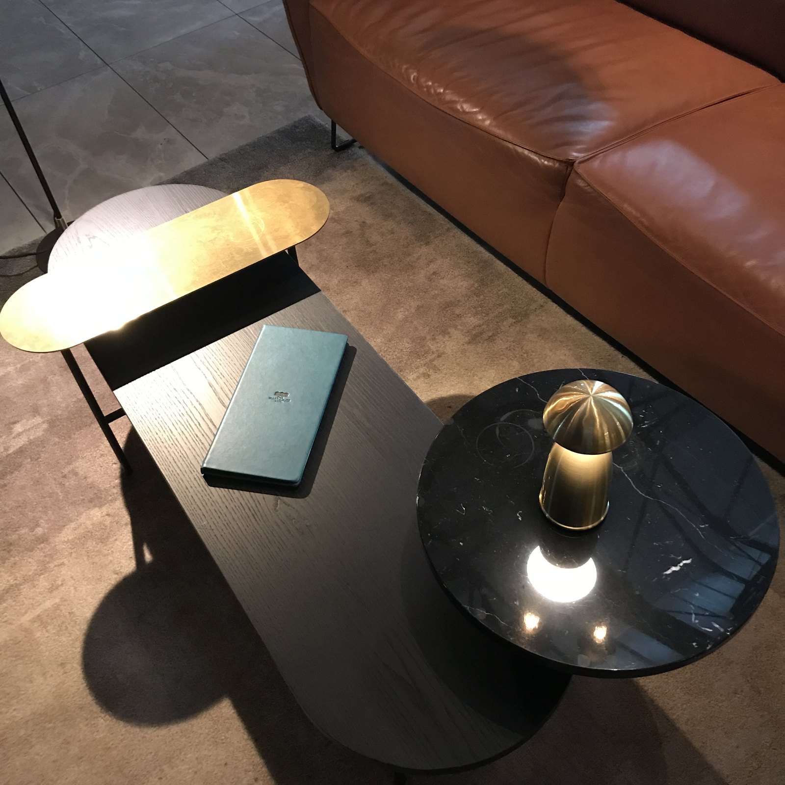 A tan leather sofa with a brass table lamp on a black marble side table and a book beside it