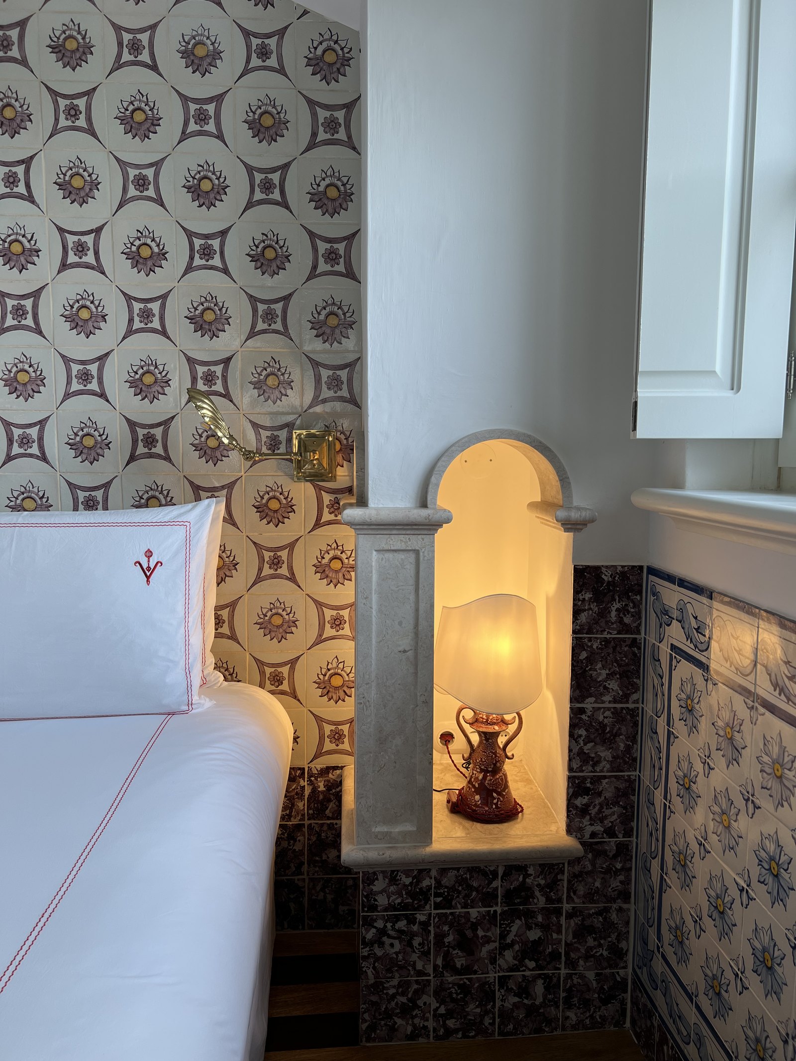 A lit lamp in a tiled alcove beside the head of a bed