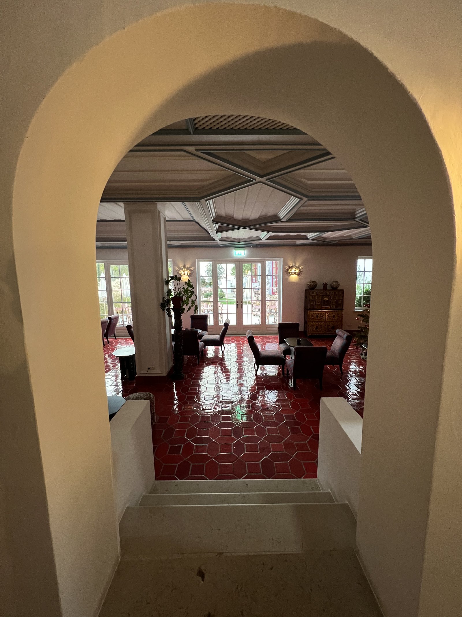 A thick white arch framing a room beyond with a deep red tiled floor