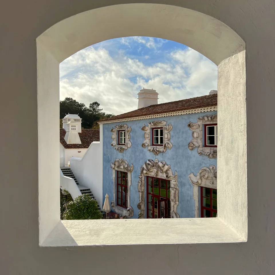 A thick arched window framing the pale blue carved facade of the building opposite