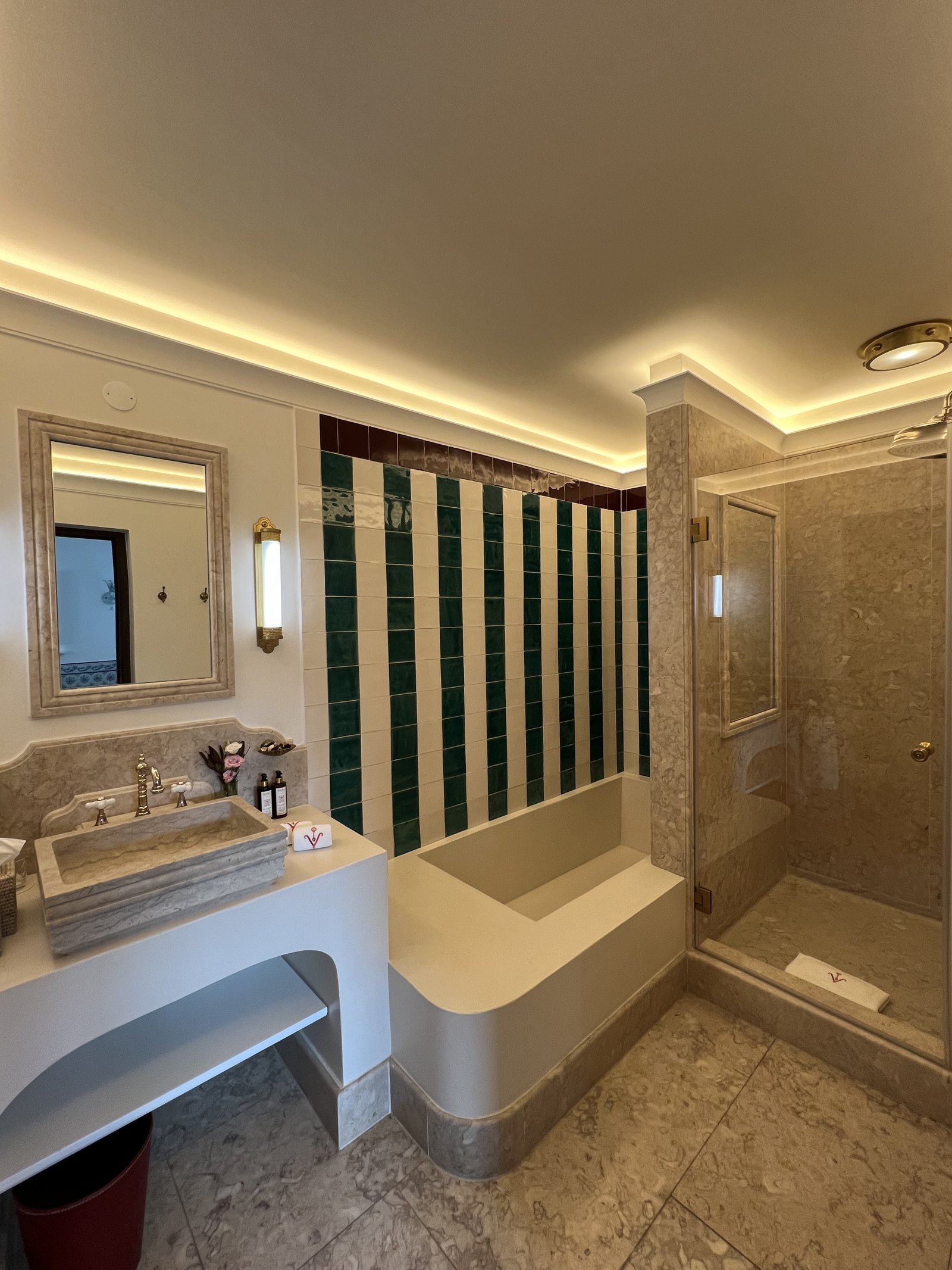 A bathroom at Vermelho with green and white striped tiling, a marble surround and a deep tub
