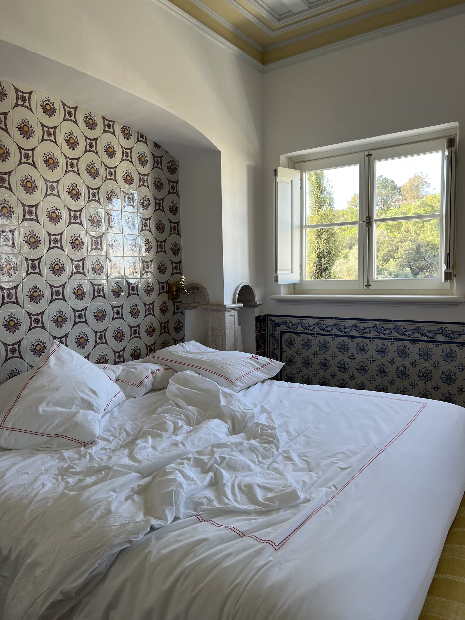 An unmade bed in the morning light with the tiled headboard behind it