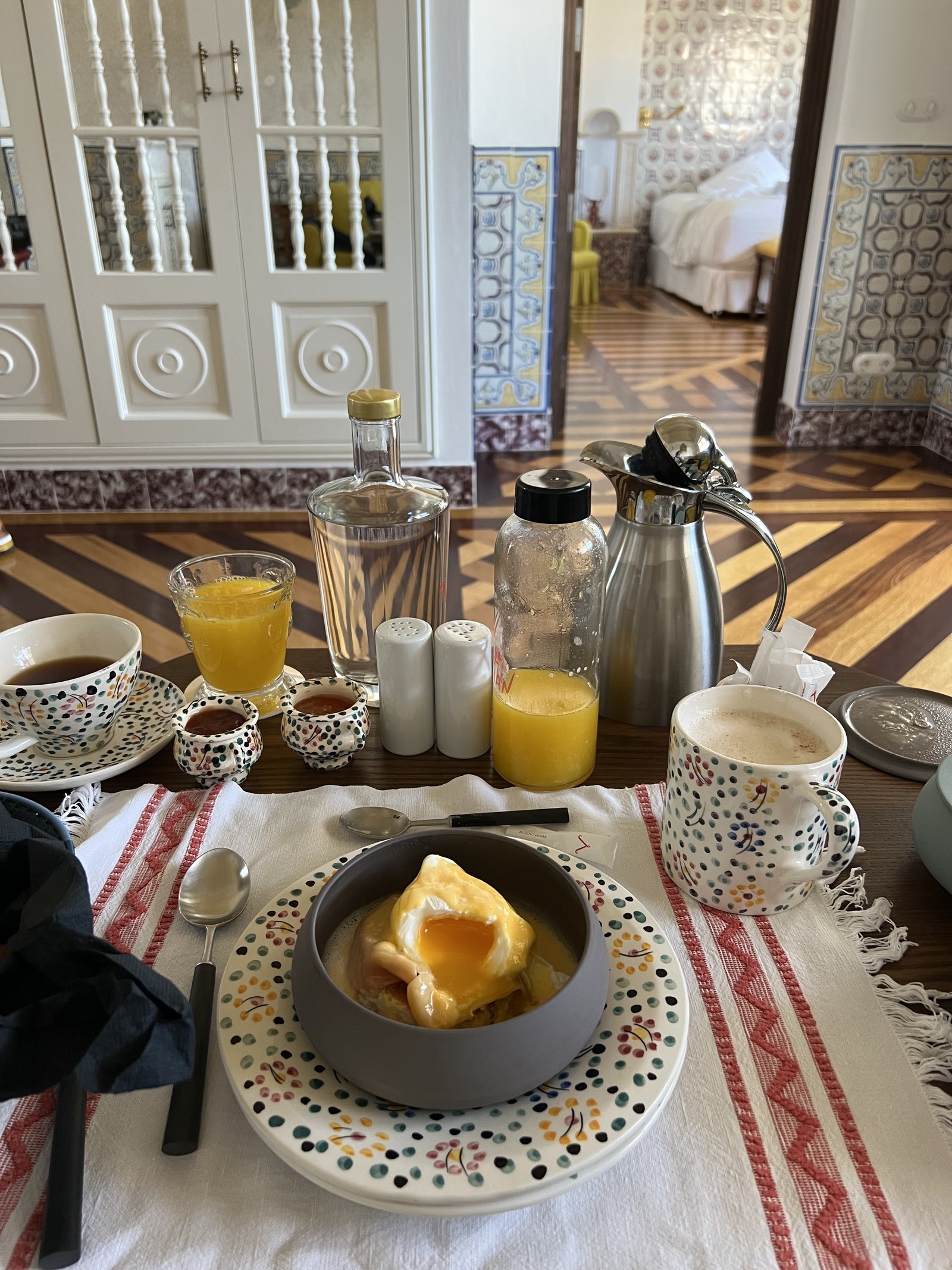 A breakfast tray with juice, coffee, bread and preserves laid out on a patterned cloth