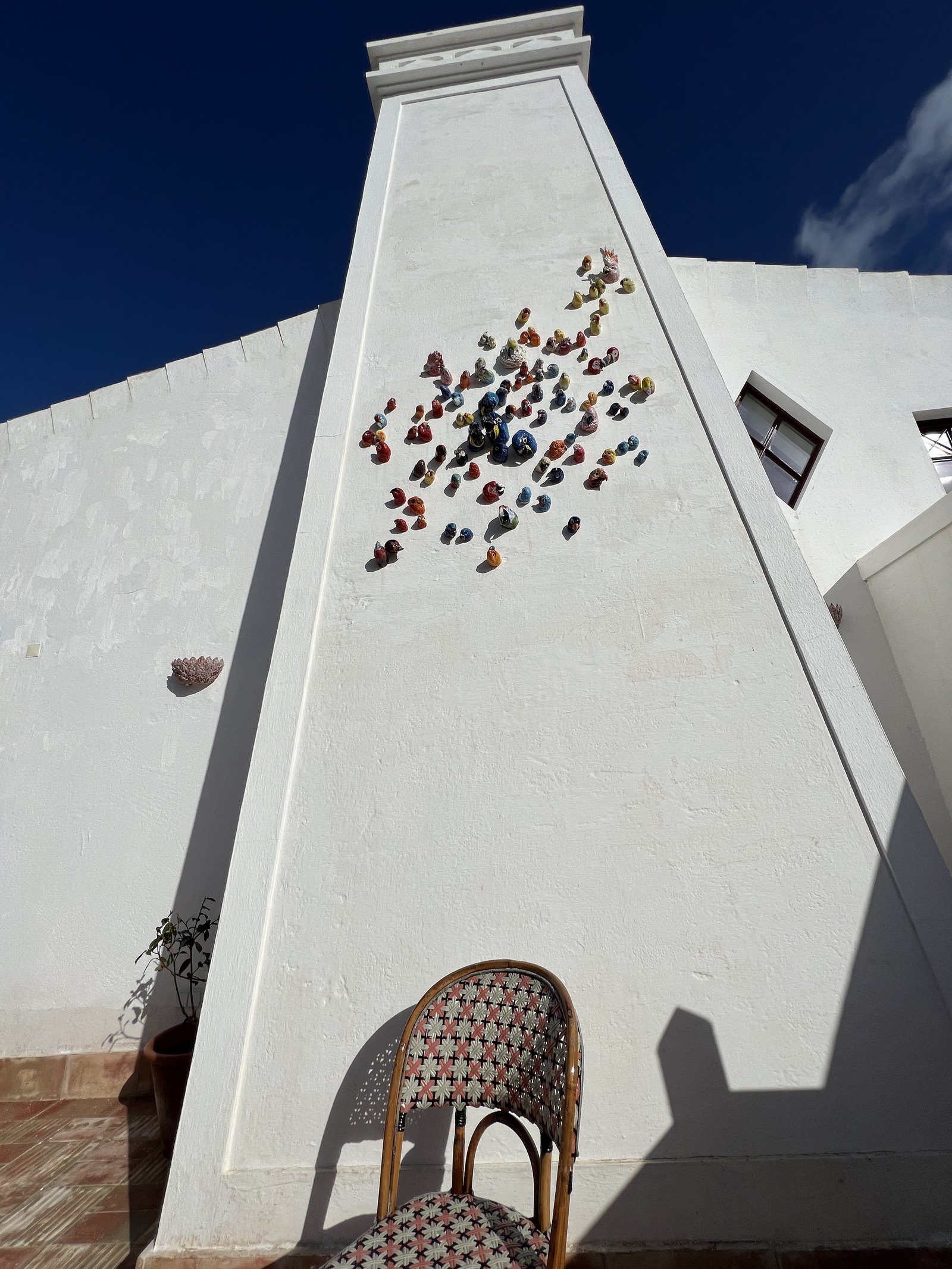 A white chimney with a scatter of small dark ceramic birds fixed to it against a deep blue sky