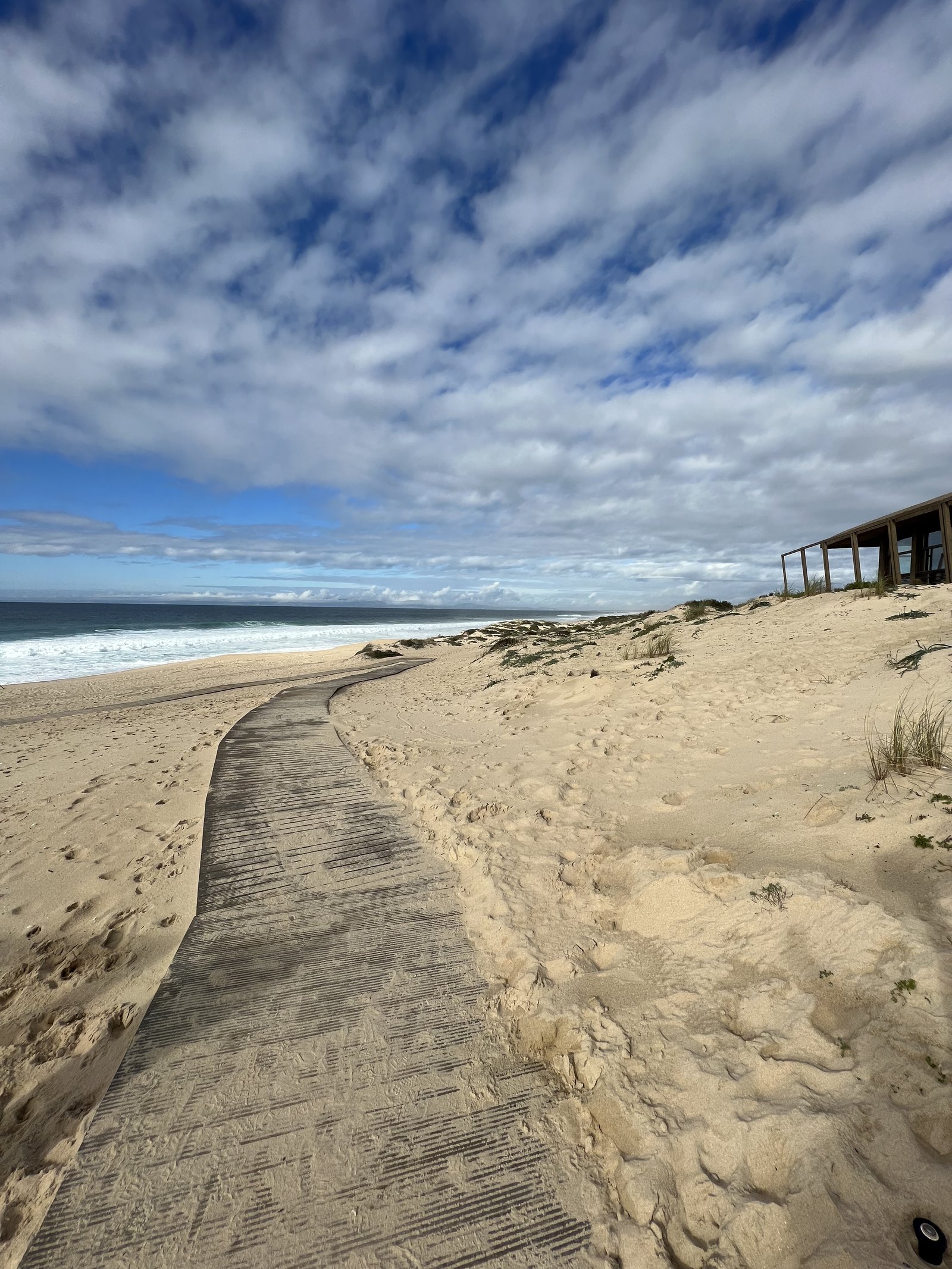 A boardwalk crossing the dunes at Comporta towards the Atlantic under a wide cloudy sky