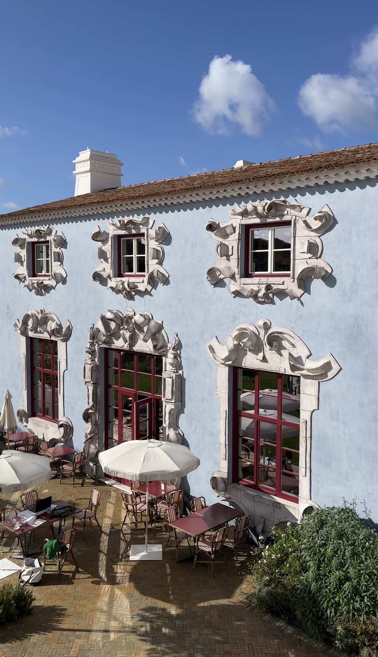 The pale blue facade of Vermelho with its carved stone window surrounds, above a terrace of fringed parasols and bistro chairs