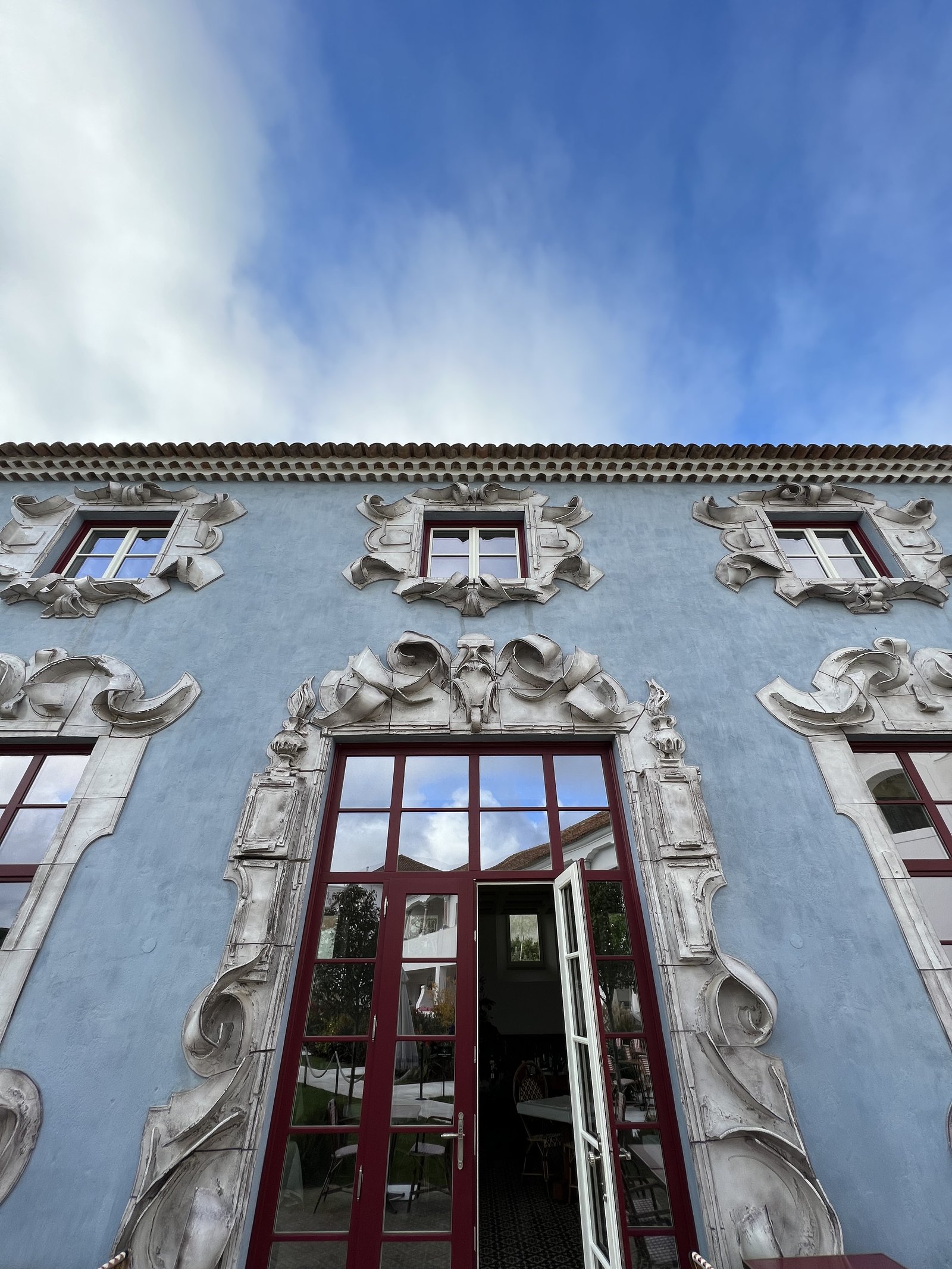 Looking up the pale blue facade of Vermelho to the carved window surrounds against the sky