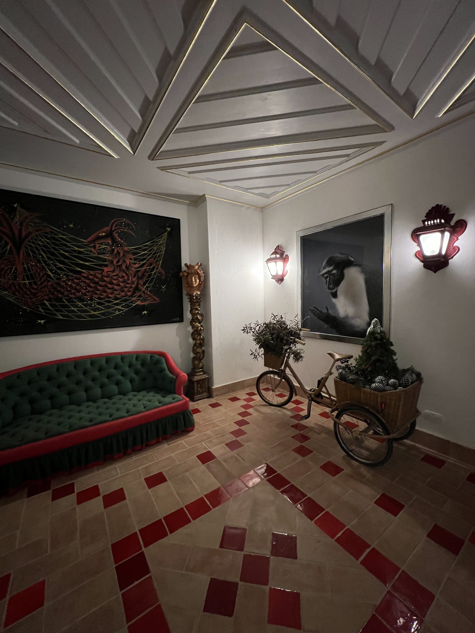 A room with a deep green sofa, a red and white diamond floor and a bicycle propped against the wall