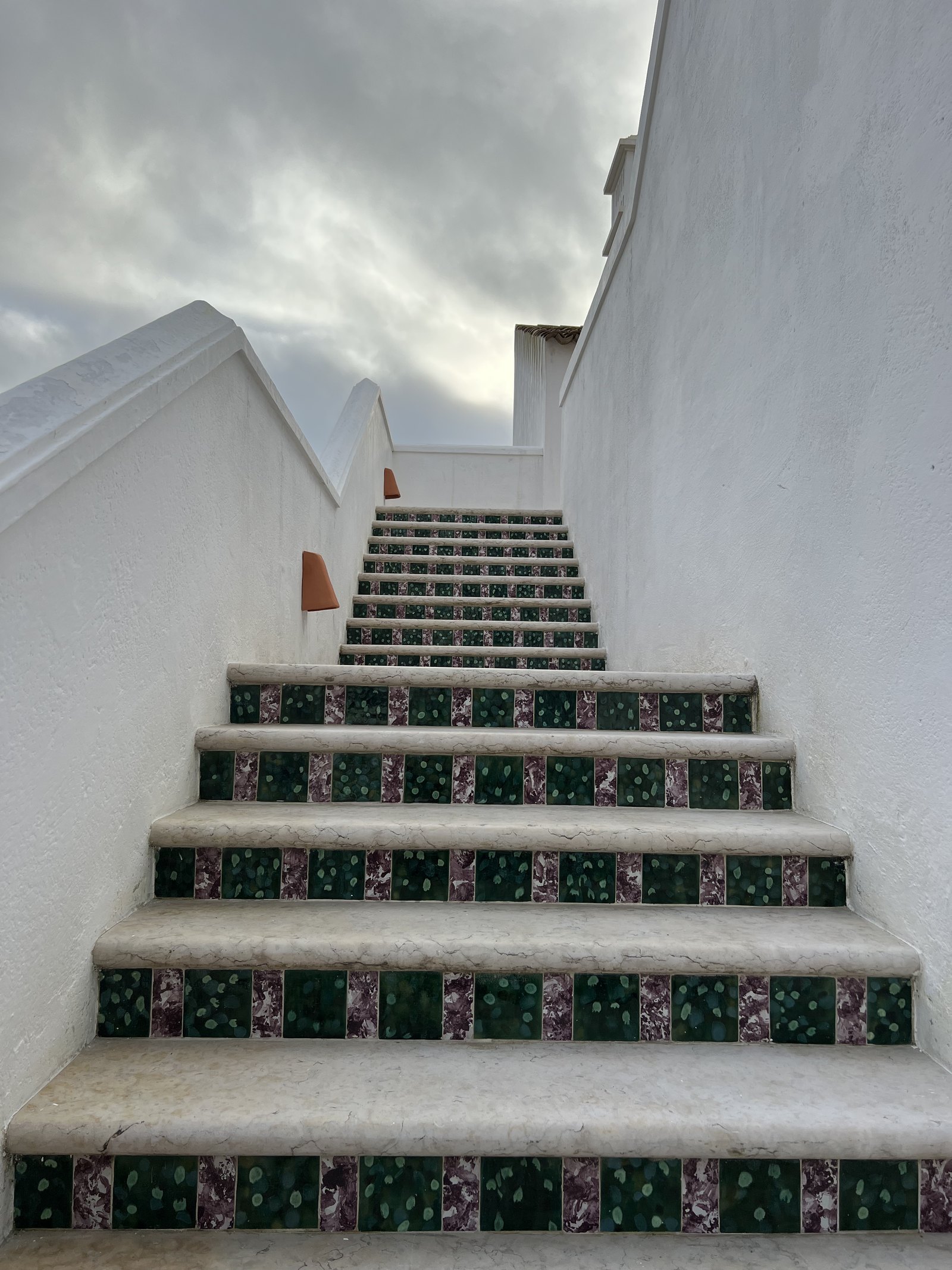 A whitewashed staircase with green patterned tiles set into each riser