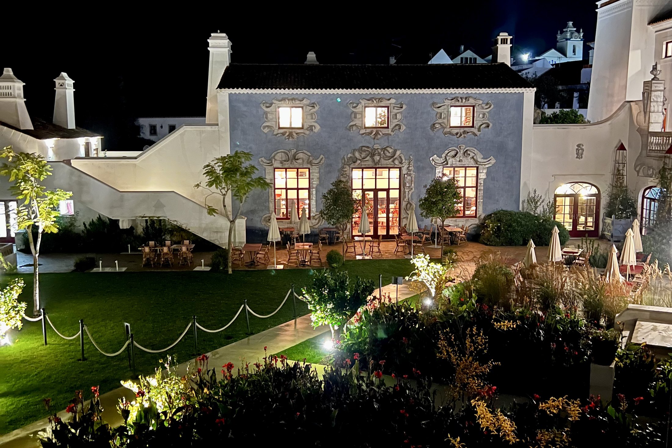 Vermelho lit from the garden at night, with the lawn and flowerbeds in front of the blue facade