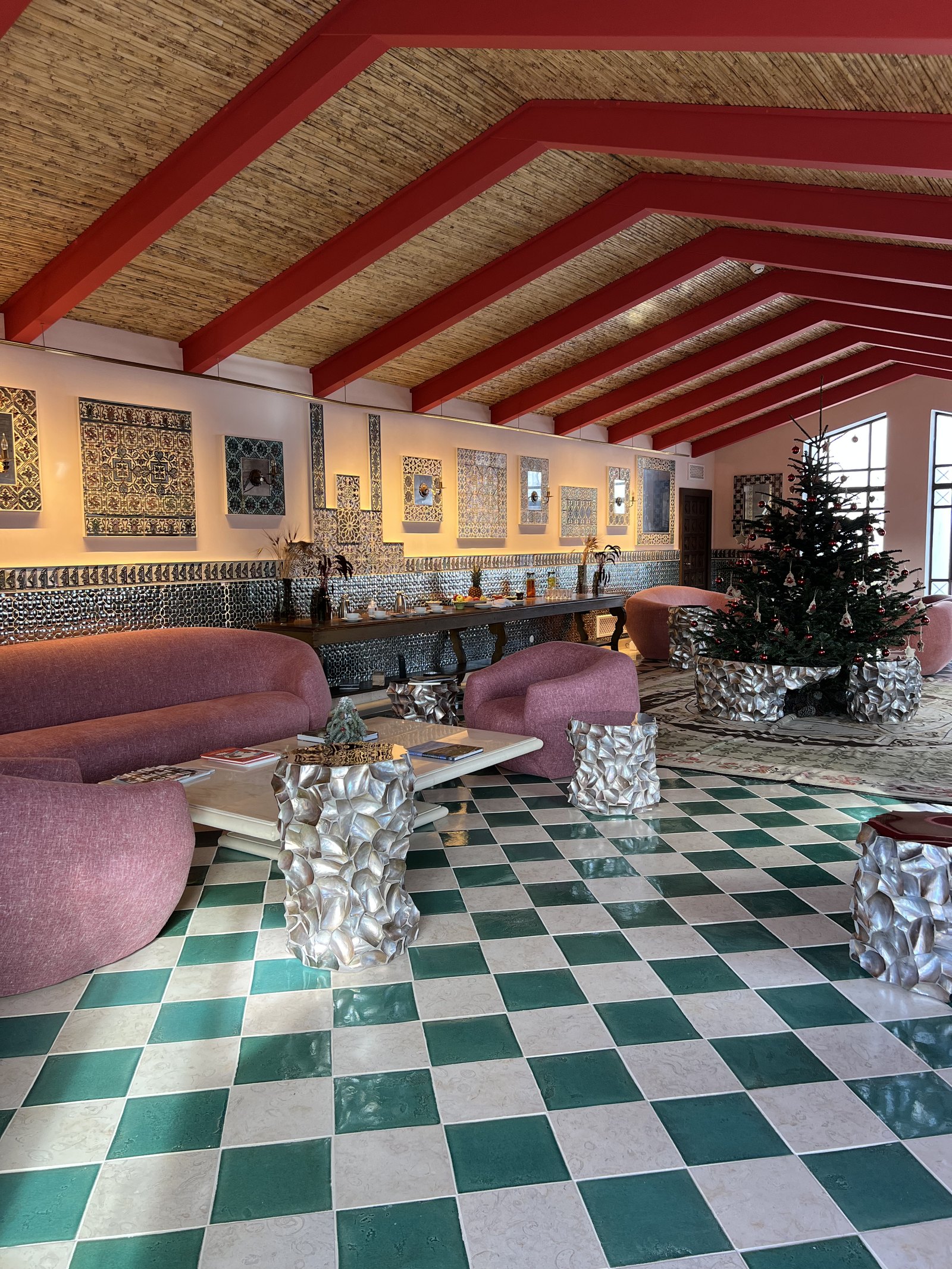 The Indian Lounge at Vermelho with red beams under a bamboo ceiling and pink velvet seating on a green and white checkerboard floor