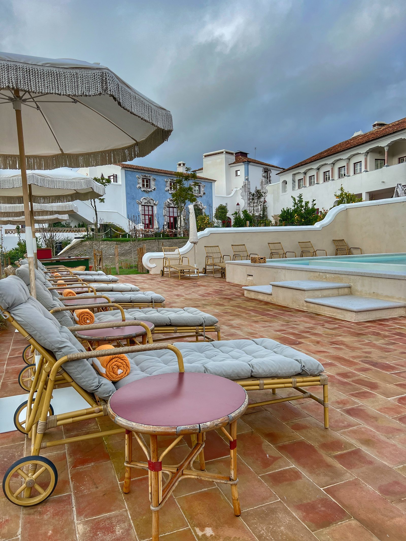 Sun loungers and a fringed parasol on a terracotta terrace above the pool