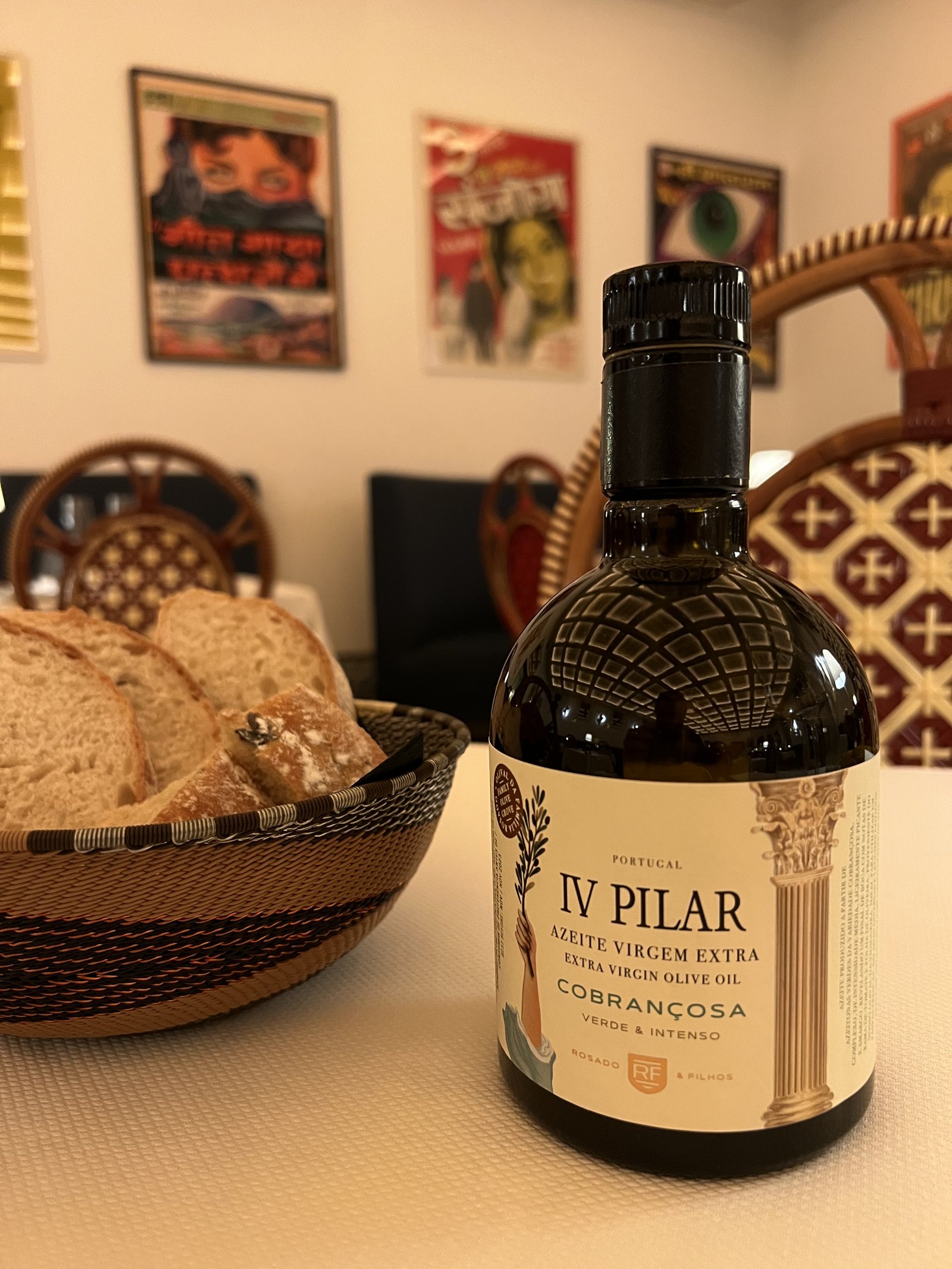 A bottle of Portuguese olive oil standing beside a basket of bread on a patterned table at Xtian