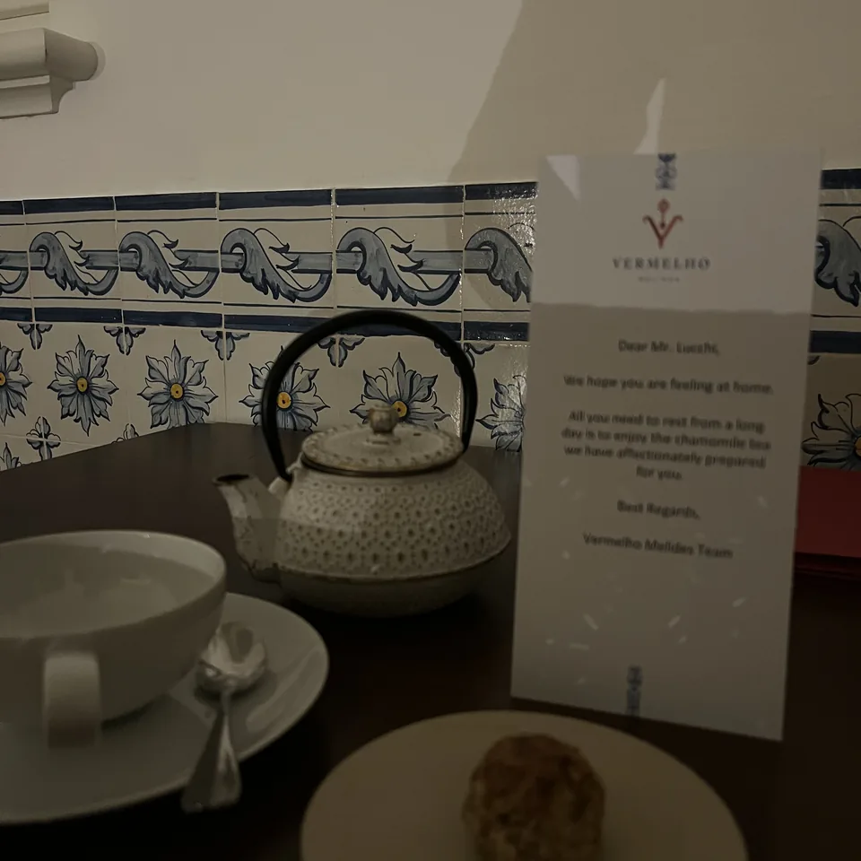 A white ceramic teapot and a handwritten card from the hotel on a dark table