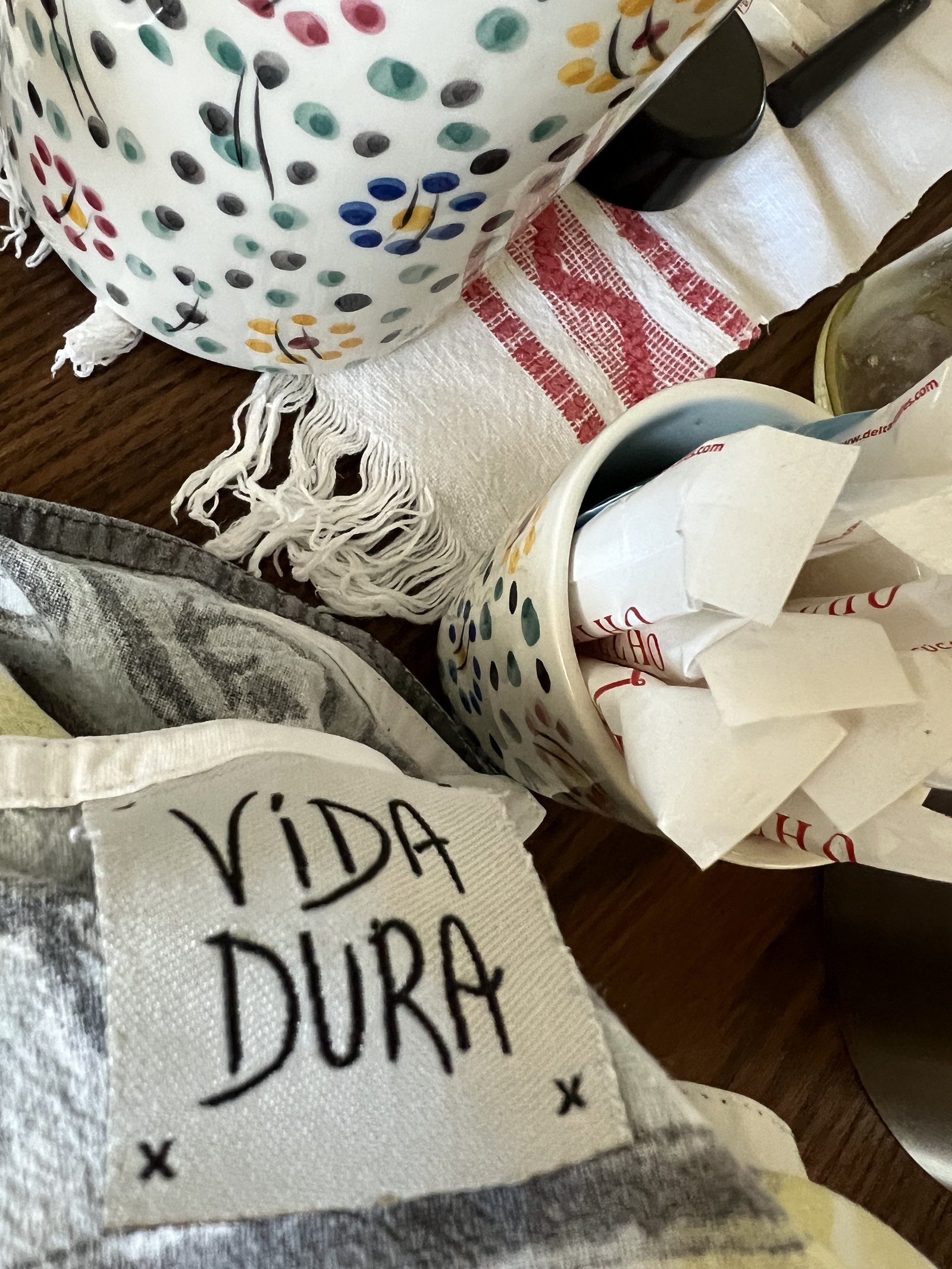 A cushion embroidered with the words Vida Dura beside painted ceramics on a table