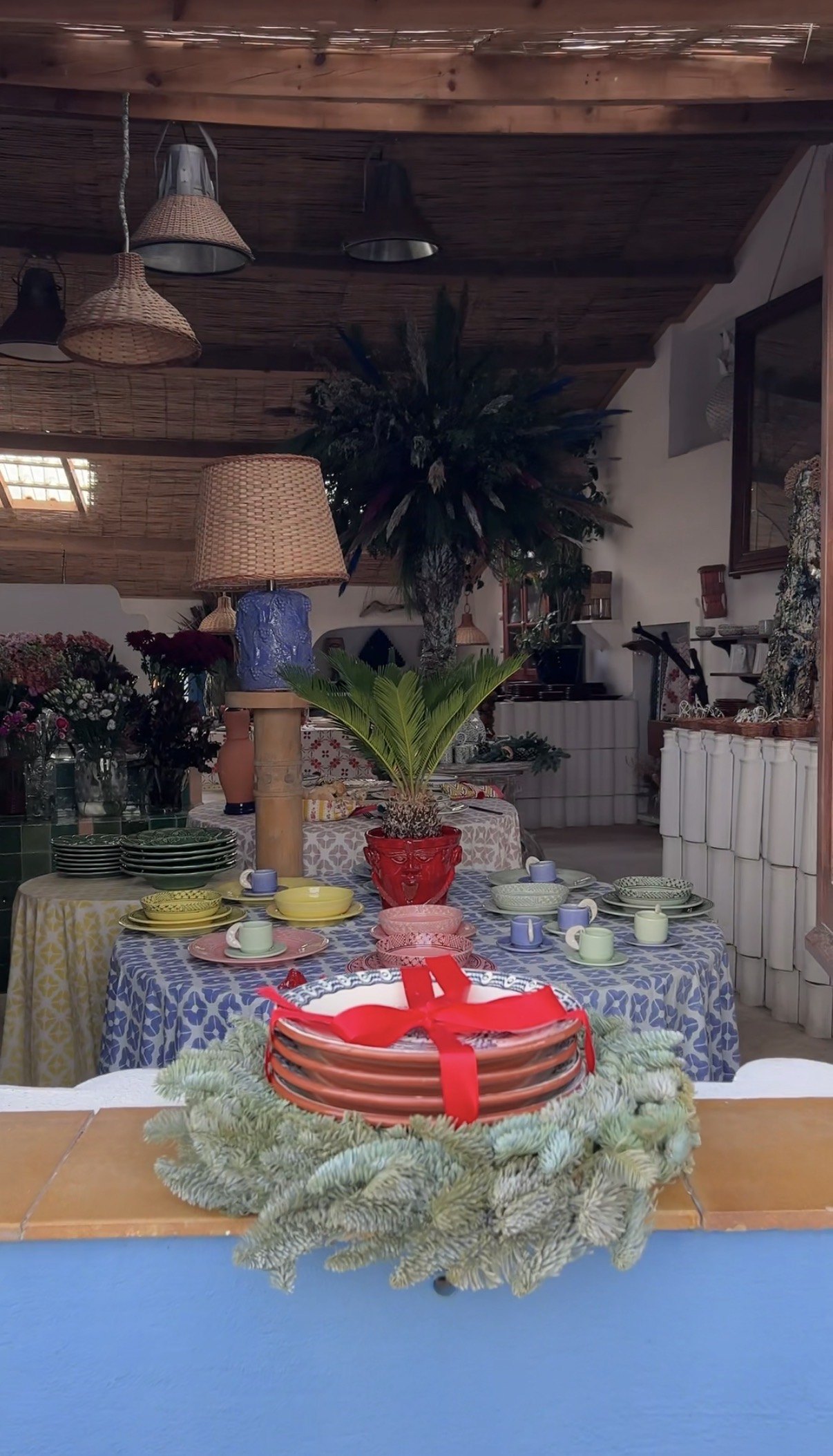 The interior of a small Melides shop with hand-painted ceramics laid out on cloth covered tables under a bamboo ceiling