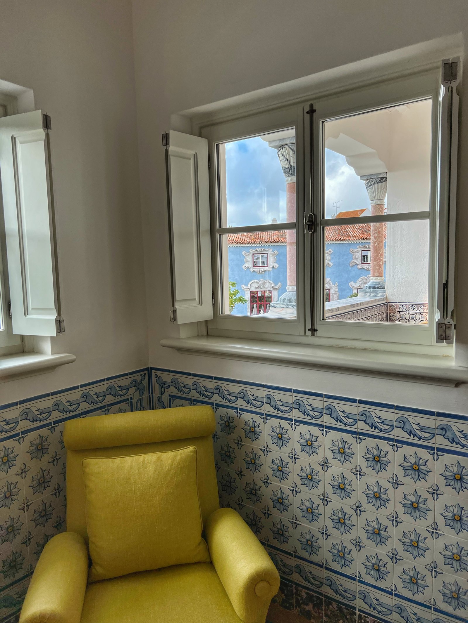 A yellow armchair in a corner under a window, above a dado of blue and white azulejos