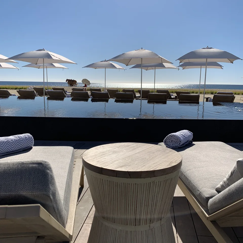 A cushioned daybed and a round timber table under a parasol at Viceroy Los Cabos, with the pool and more parasols behind