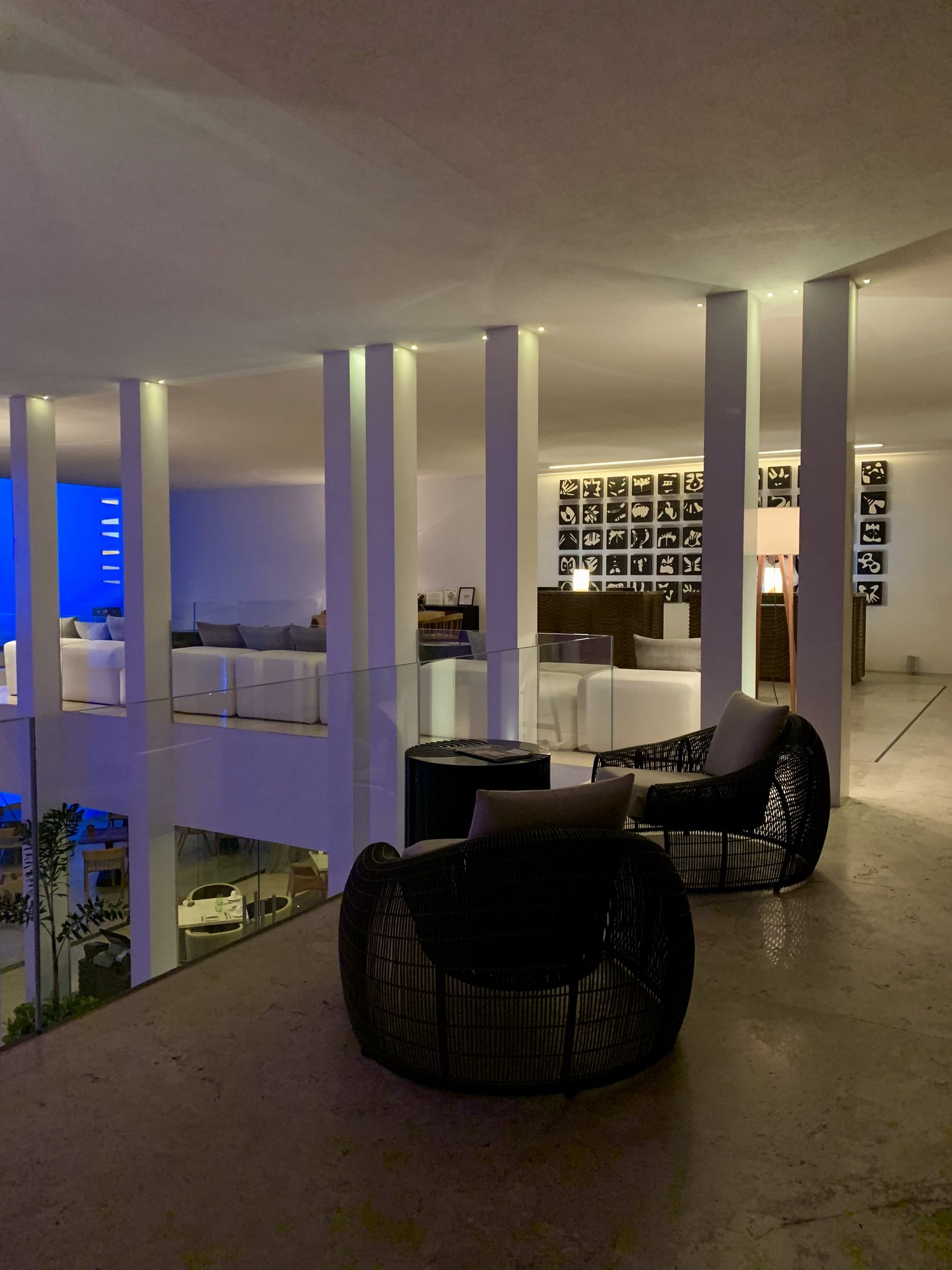 The lobby at Viceroy Los Cabos after dark with a single woven chair in the foreground and the walls lit blue behind the columns