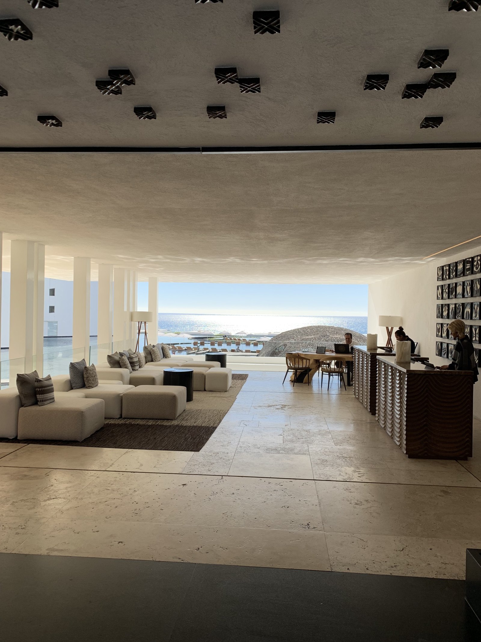 The open lobby at Viceroy Los Cabos with pale sofas and a timber floor running to an opening with no wall, looking out to the pools and the sea