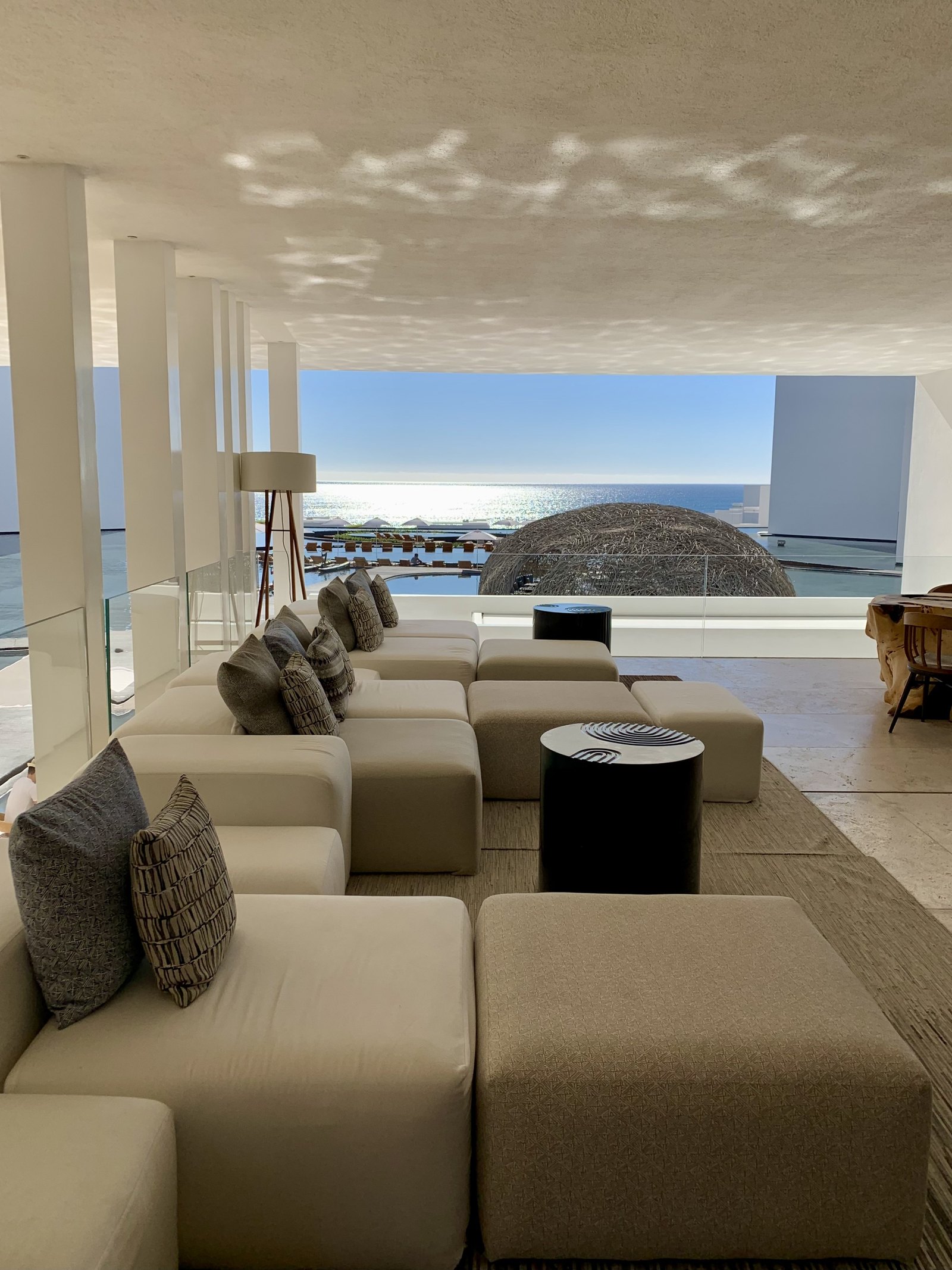 Low sand-coloured sofas in the lounge at Viceroy Los Cabos arranged towards a wide opening with the woven dome and the sea visible through it