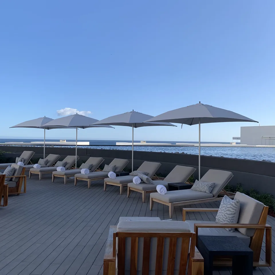 A row of loungers and grey parasols on the timber deck at Viceroy Los Cabos with the sea beyond