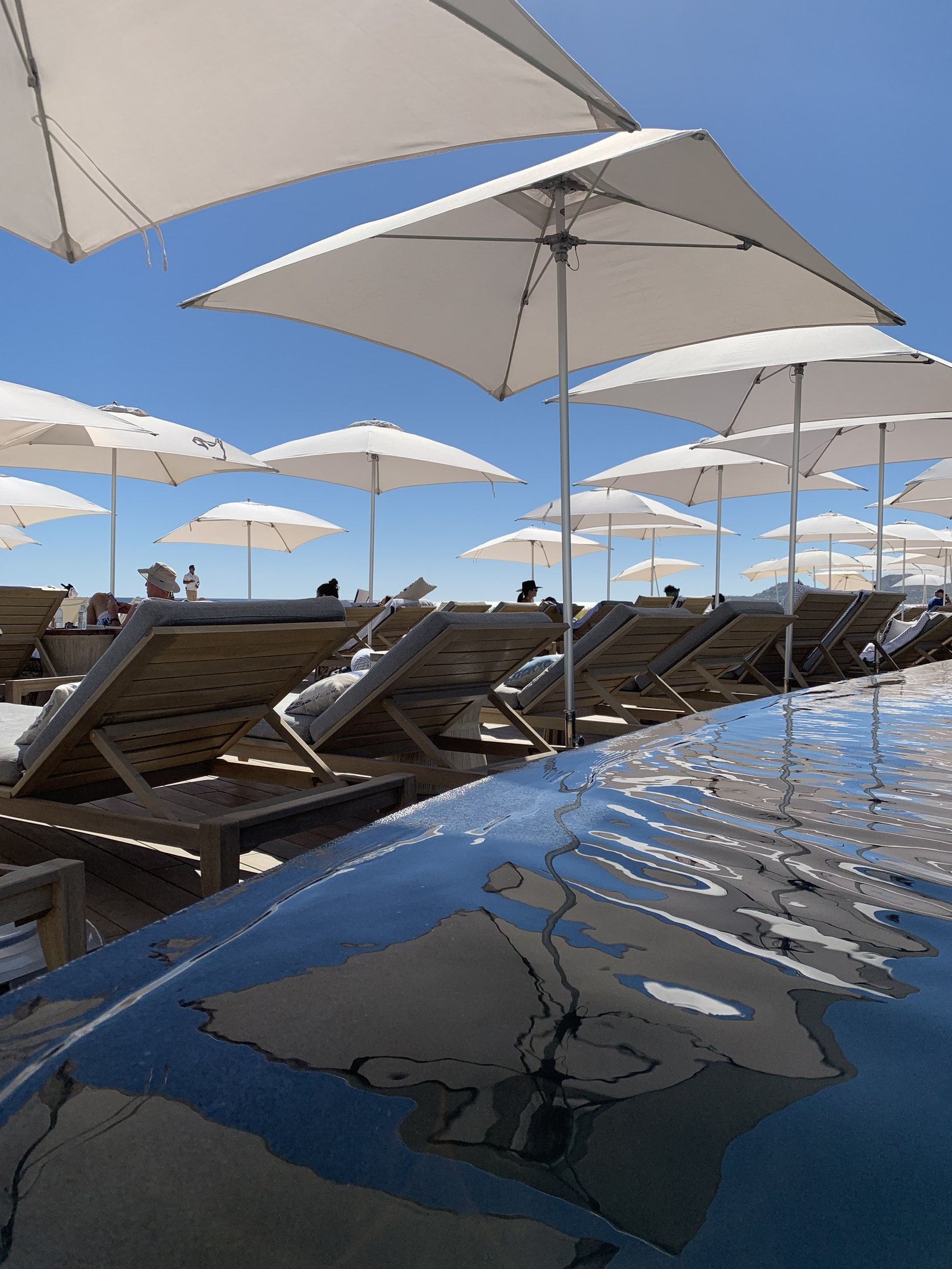A line of white parasols and loungers at Viceroy Los Cabos reflected in the dark still water beside the deck
