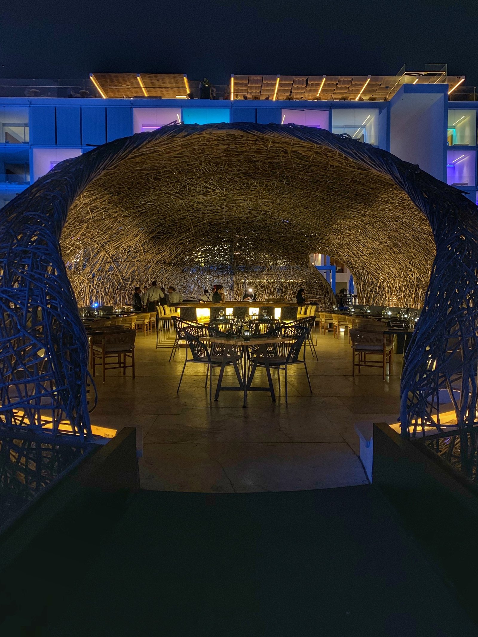 The woven dome at Viceroy Los Cabos lit gold from inside after dark, standing in black water with the blue-lit blocks of the hotel behind it