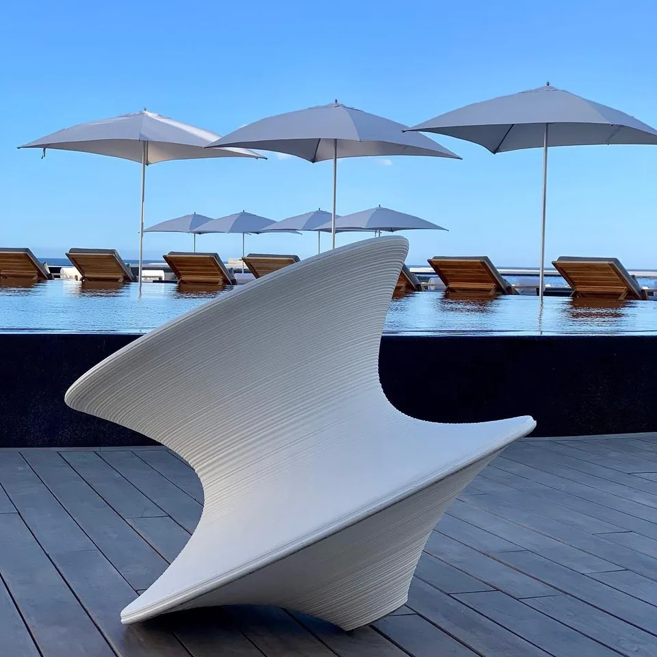 A white moulded lounger with a curved back standing on the timber deck at Viceroy Los Cabos, with parasols and the pool behind it