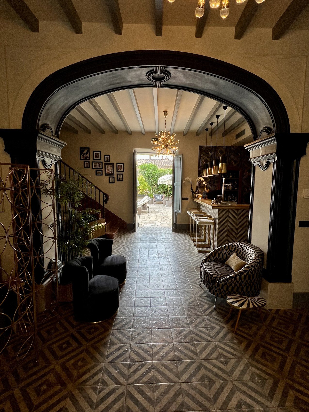 A tall arched hall with a chandelier and a patterned tiled floor running through to a courtyard