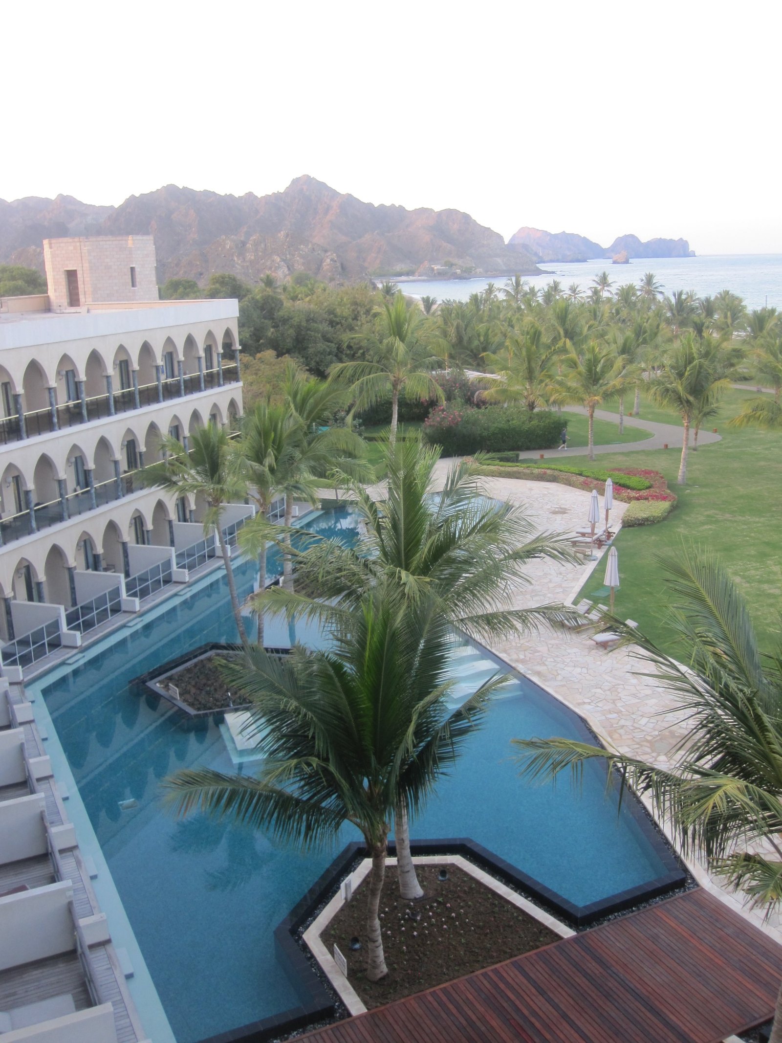 An arcaded wing of arched balconies beside angular pools set with palms, the mountains and the sea behind