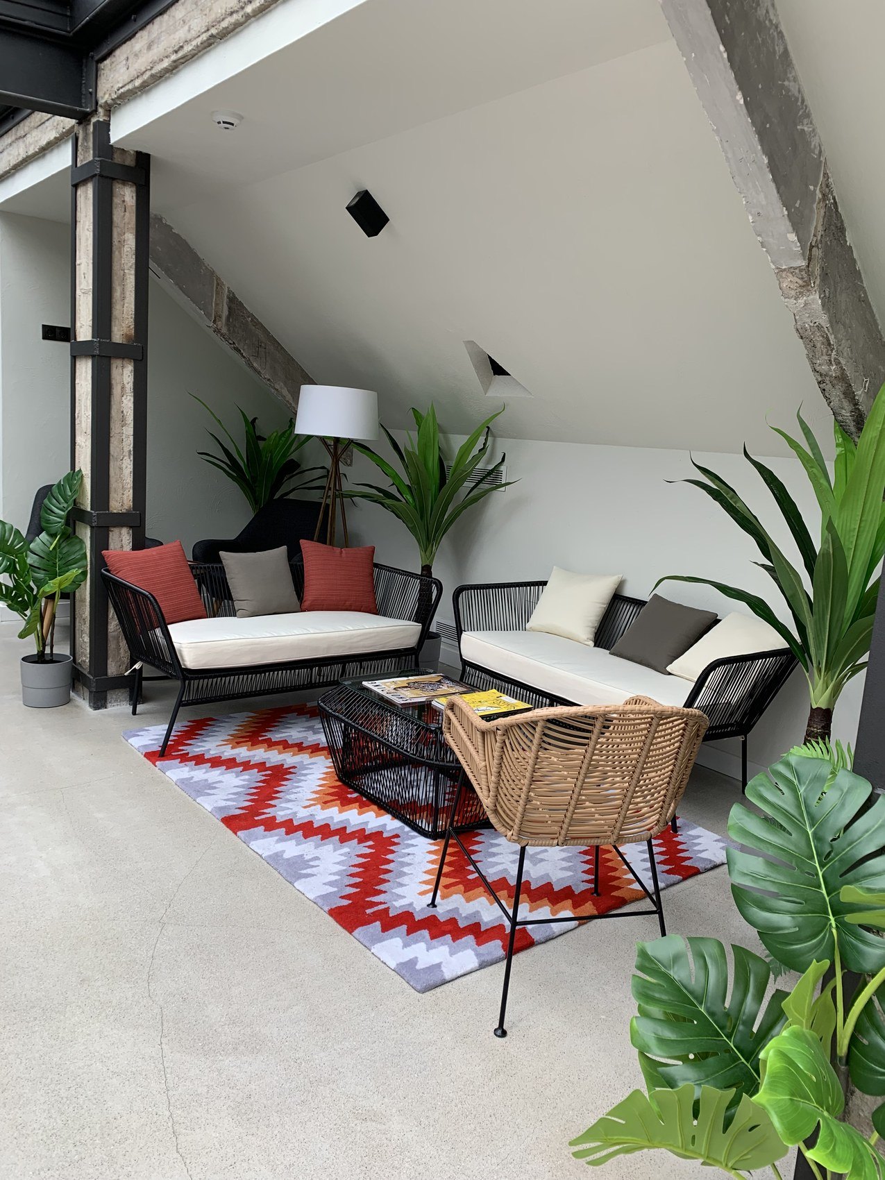 An attic sitting room under a sloped white ceiling with plants and a red patterned rug