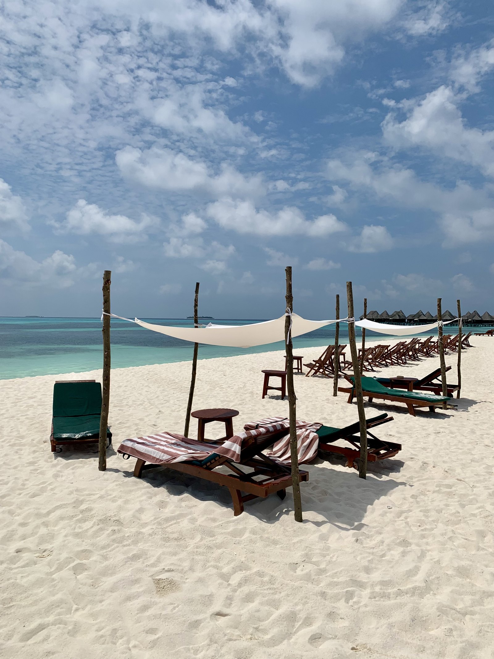 A row of timber loungers under white sail canopies on an empty beach