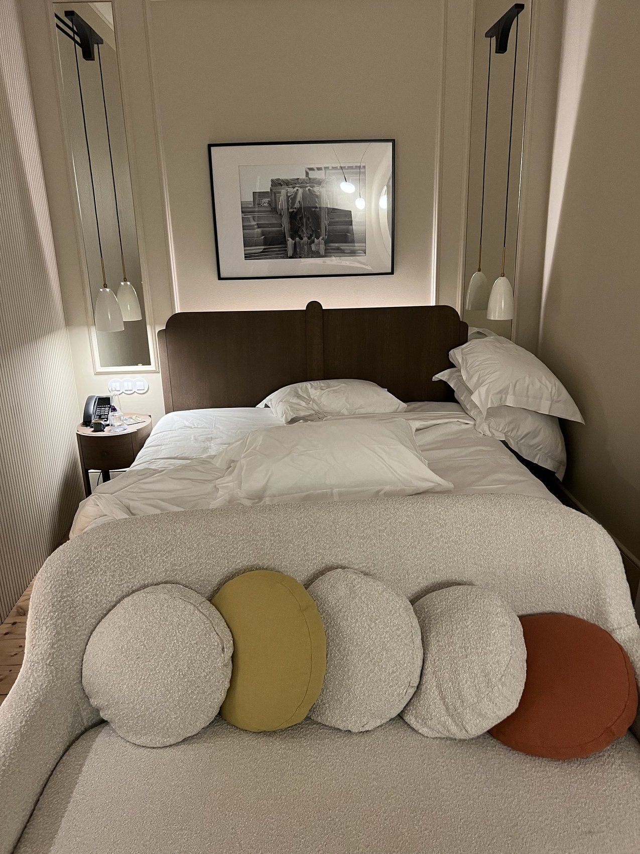 A bed with a padded headboard and a row of round cushions in white, ochre and rust