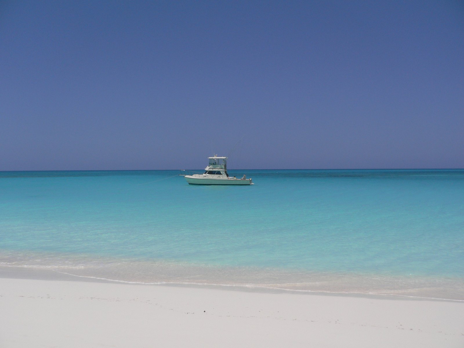 A small fishing boat at anchor on flat turquoise water off an empty white beach