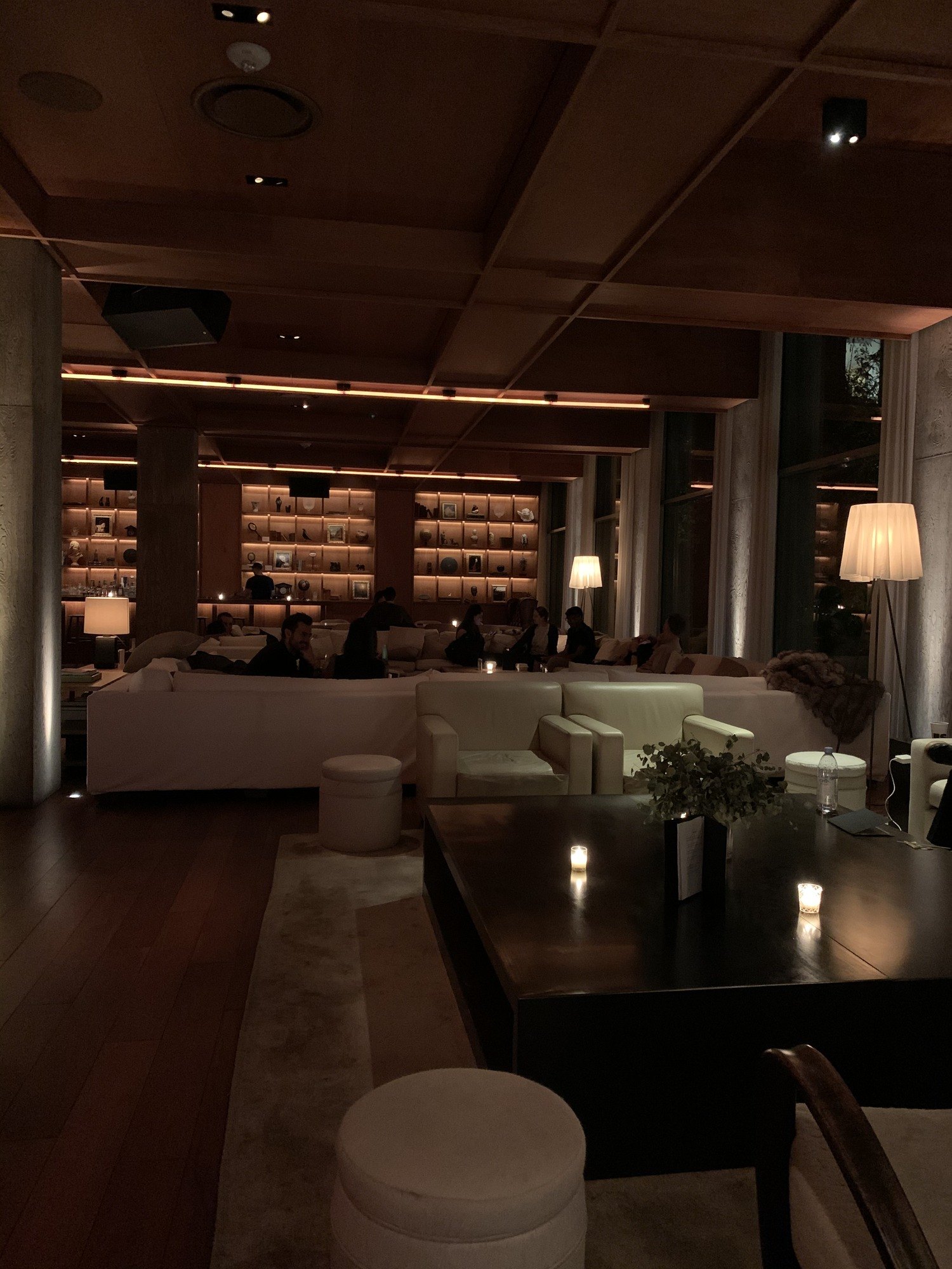 A lounge with a long wall of books, low pale sofas and a dark table in the foreground set with small candles and a sprig of greenery