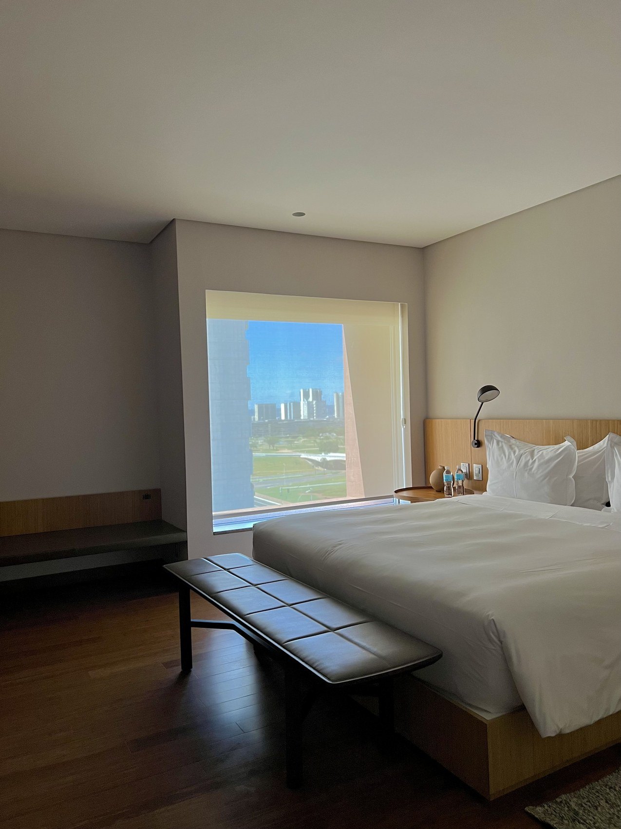 A bed and a long bench in a plain room, a tall window onto the plain beyond