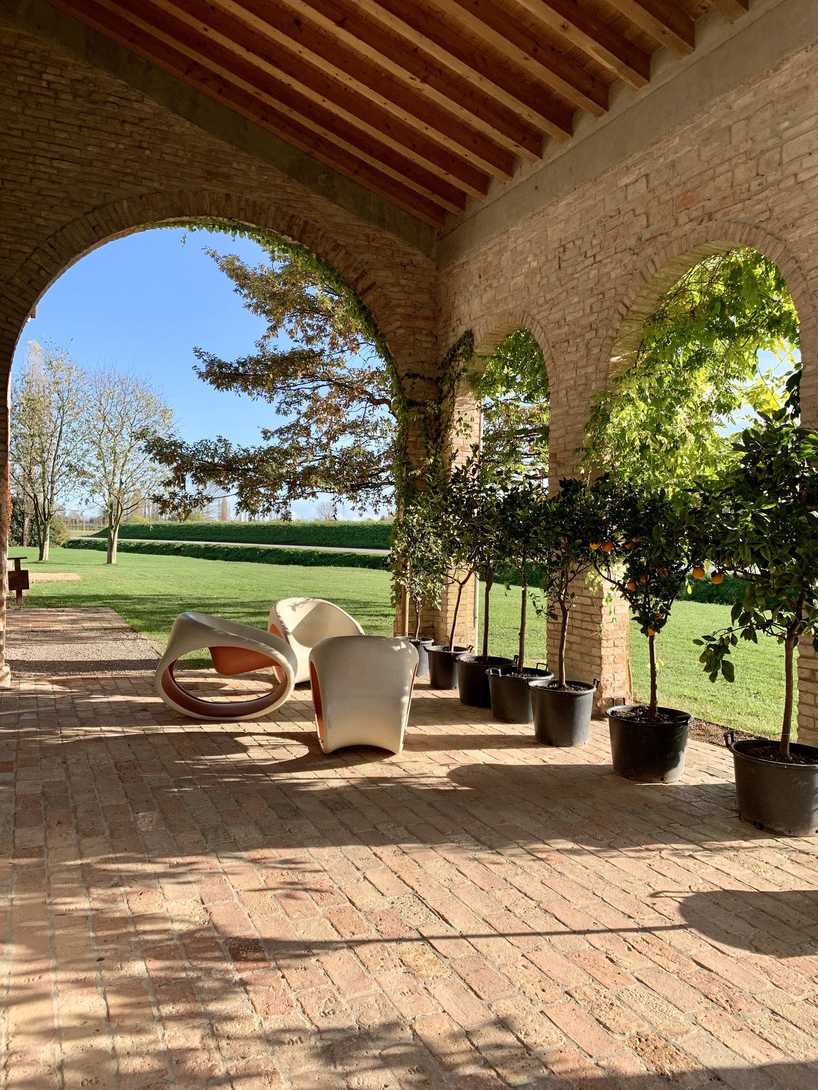 A brick arcade opening onto a lawn, with citrus trees in pots