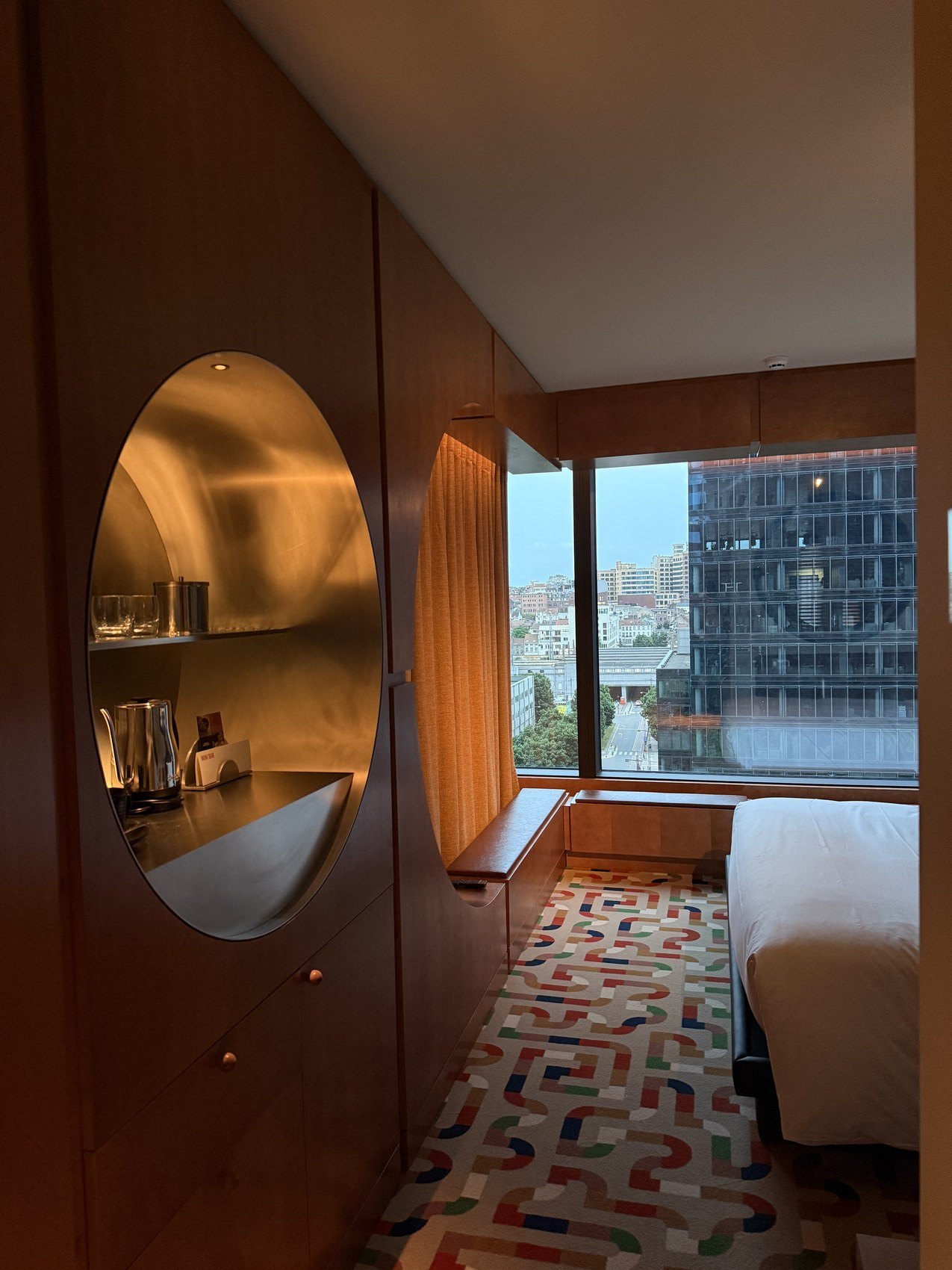 A round mirrored niche in a timber wall, the bed and the city beyond it