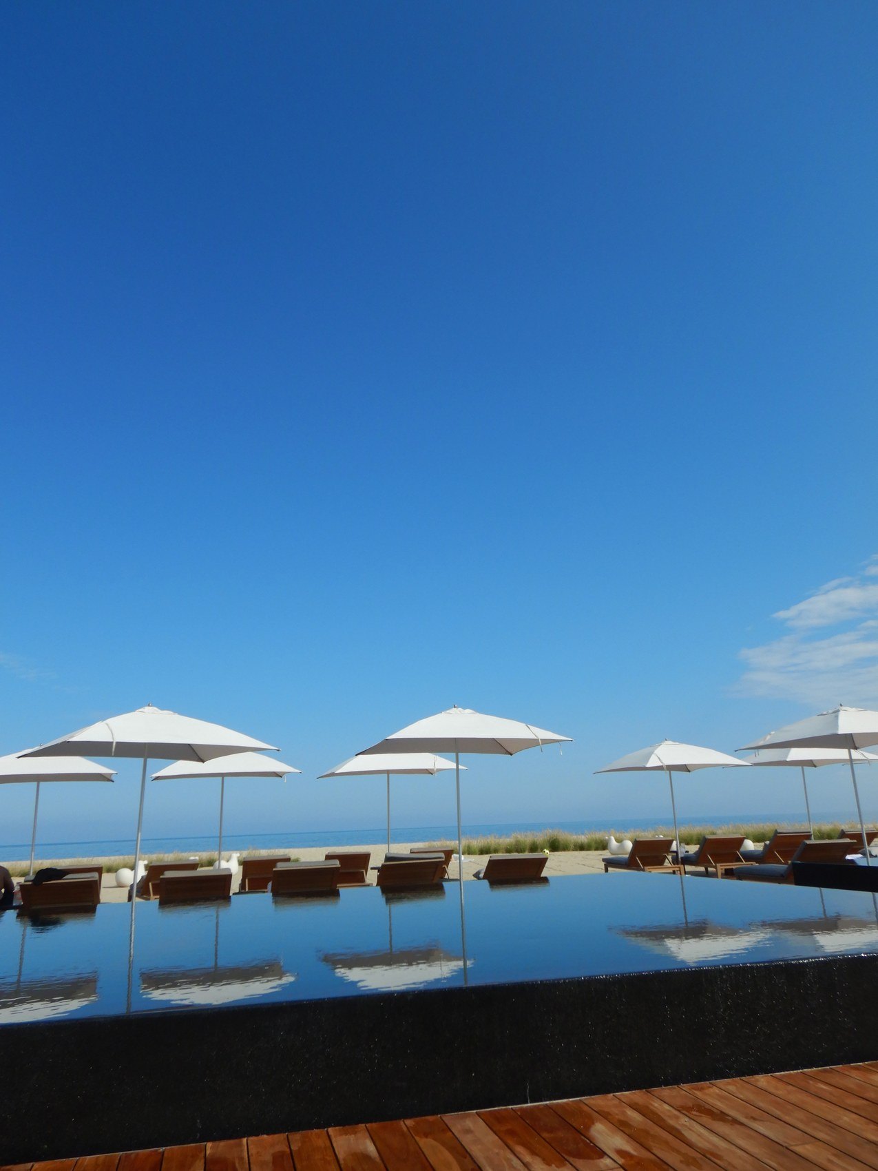 White parasols standing in a row, reflected in the still water of an infinity pool