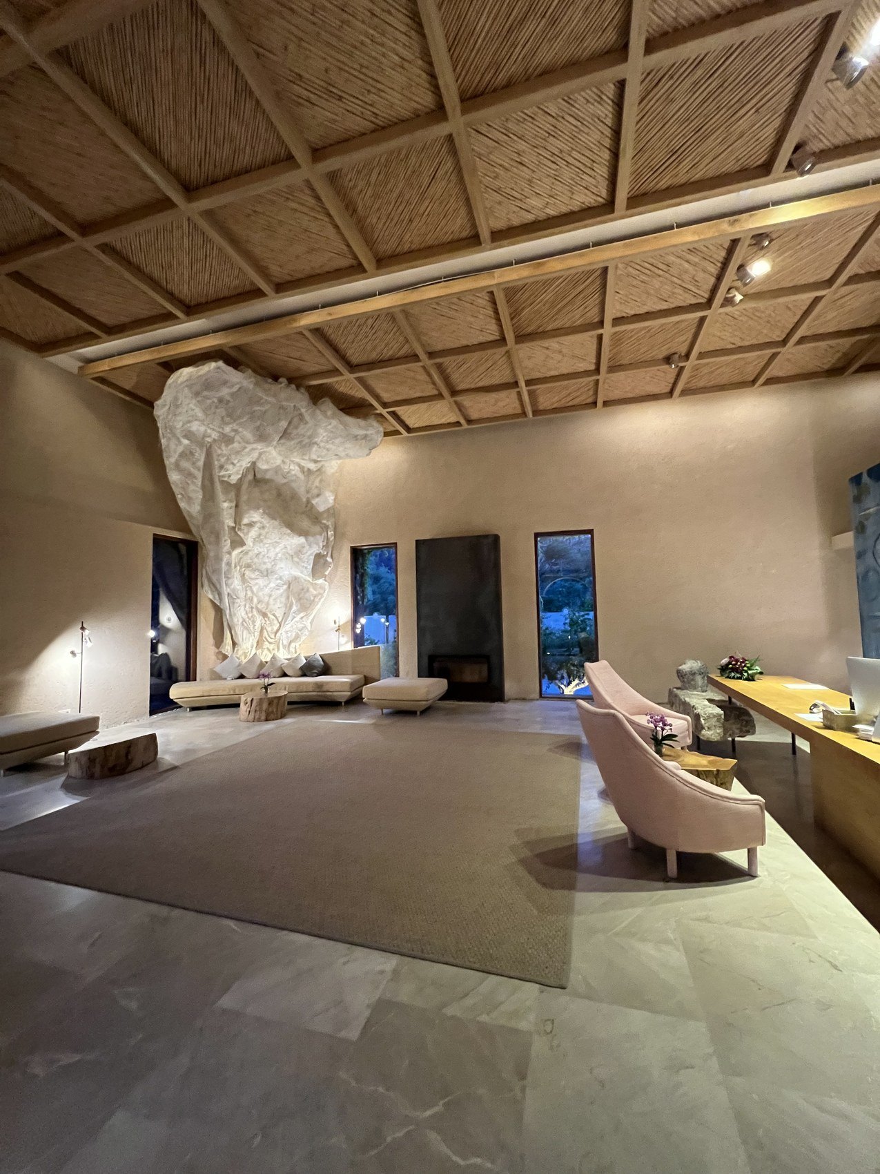 A long salon under a cane and timber coffered ceiling, with a pale rug and a stone sculpture