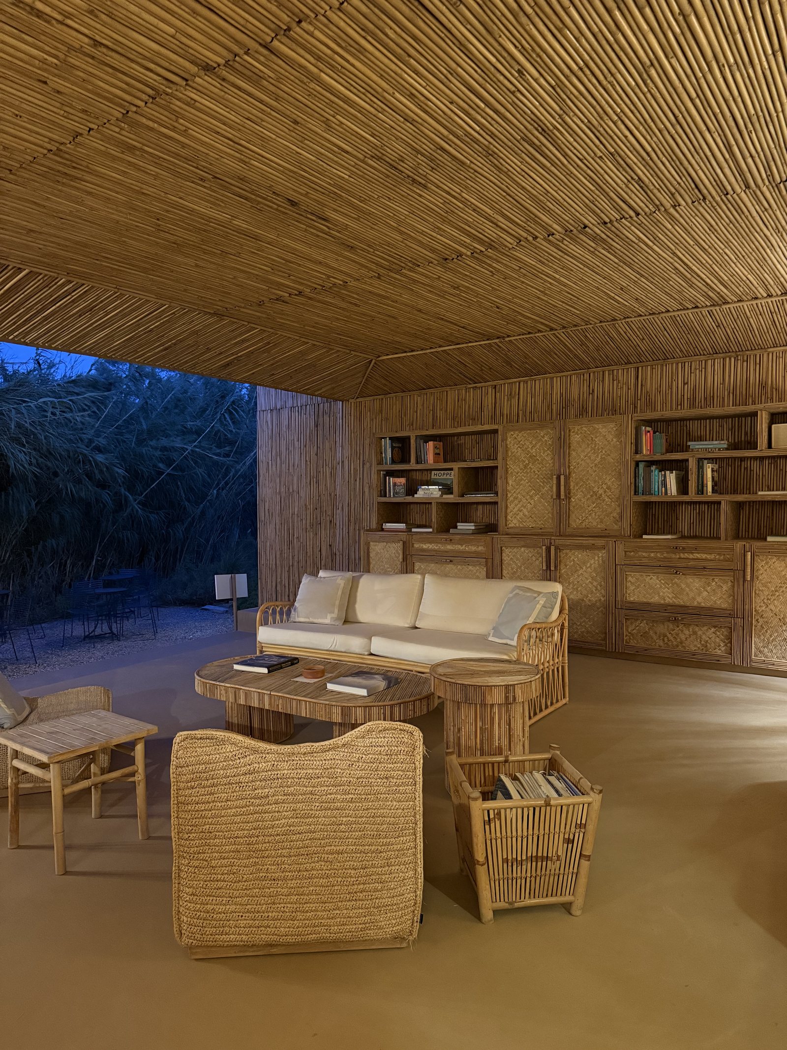 A lounge walled and ceilinged in cane, lit at dusk
