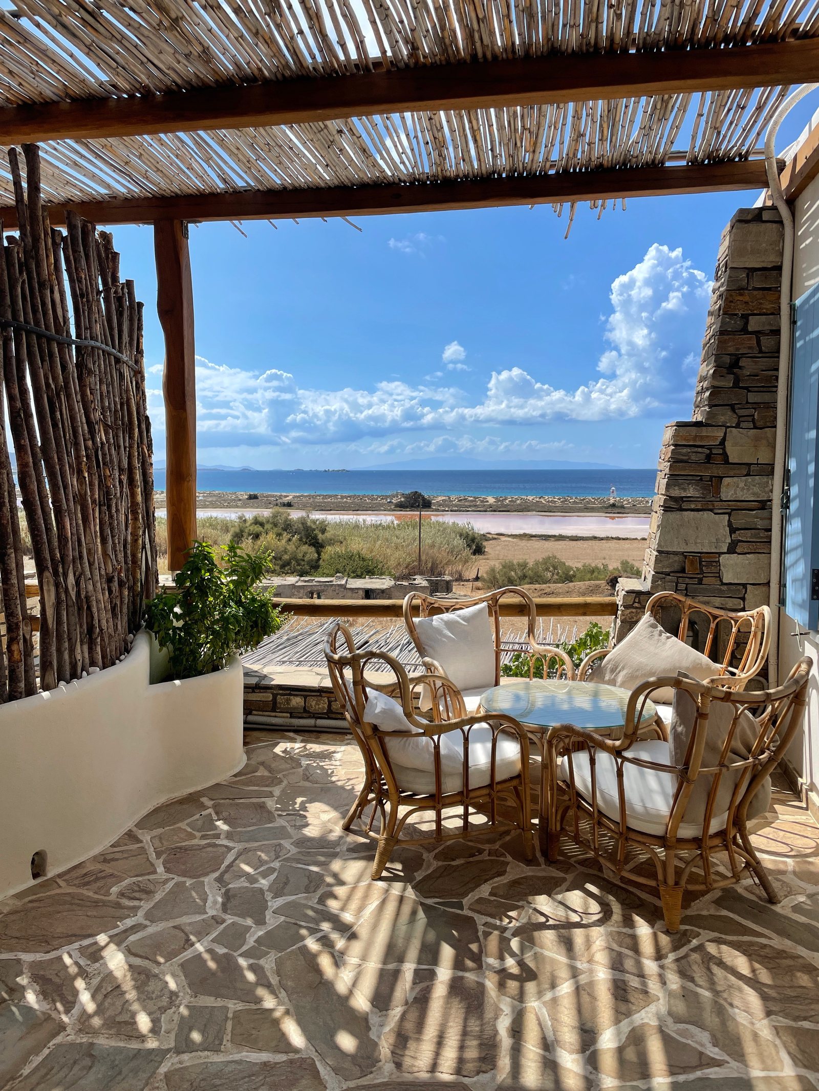 A terrace under a cane roof with wicker chairs, looking out to the water