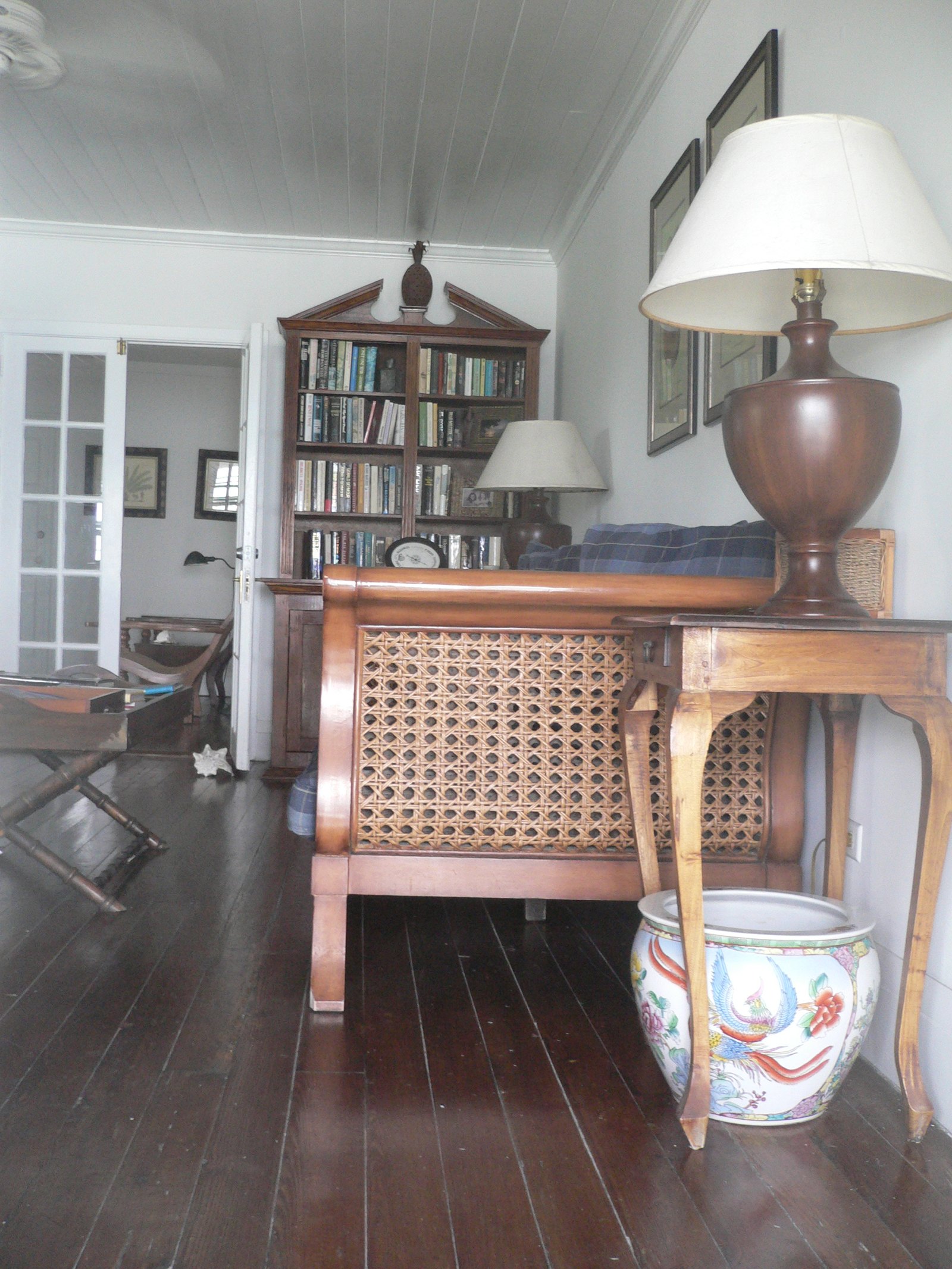 A caned sleigh sofa and a tall pedimented bookcase in a white boarded room on a dark timber floor
